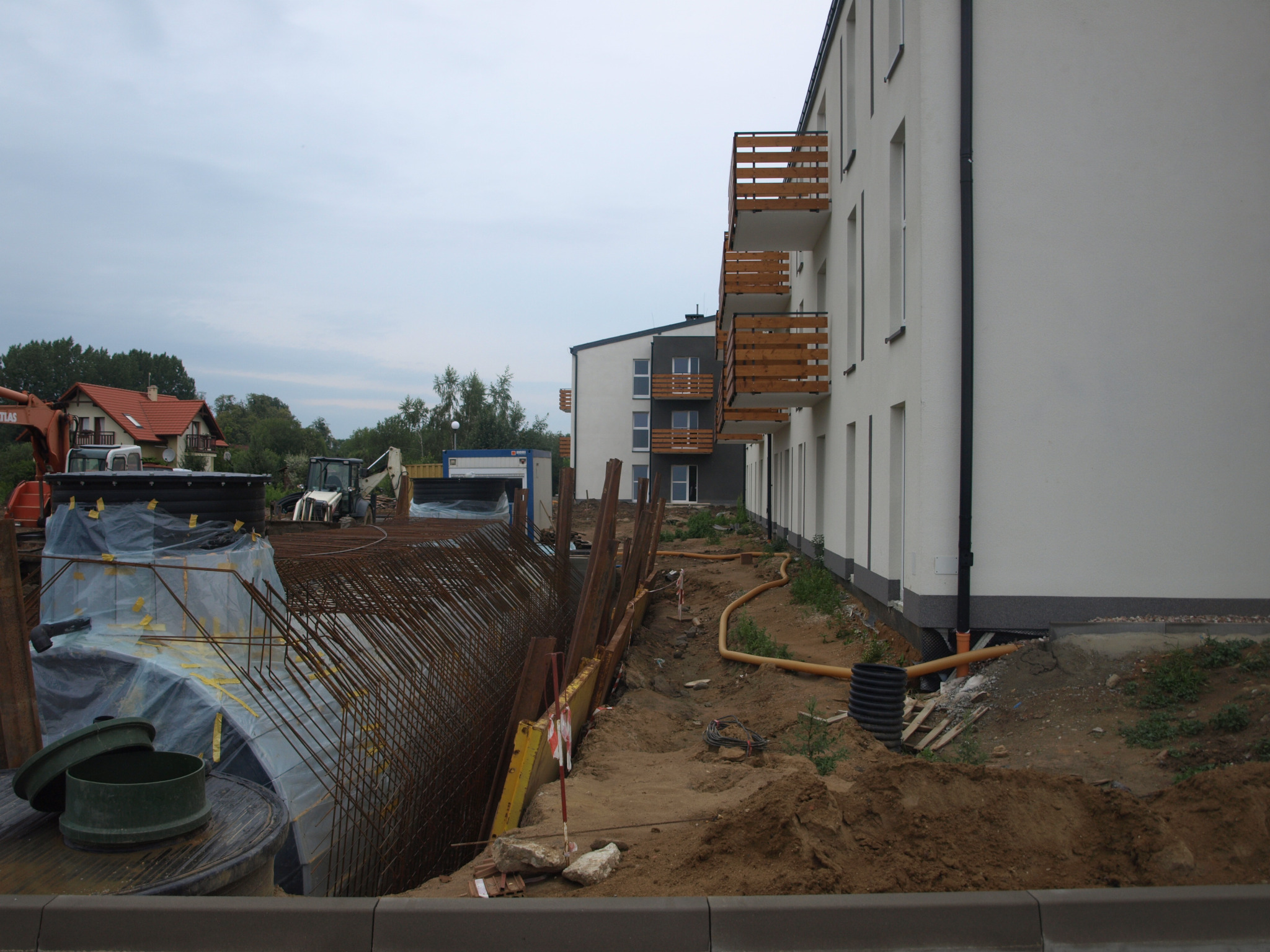 Wykonanie wykopu pod fundamenty budynku mieszkalnego, widoczne zbrojenia, szalunki oraz ciężki sprzęt budowlany w tle.