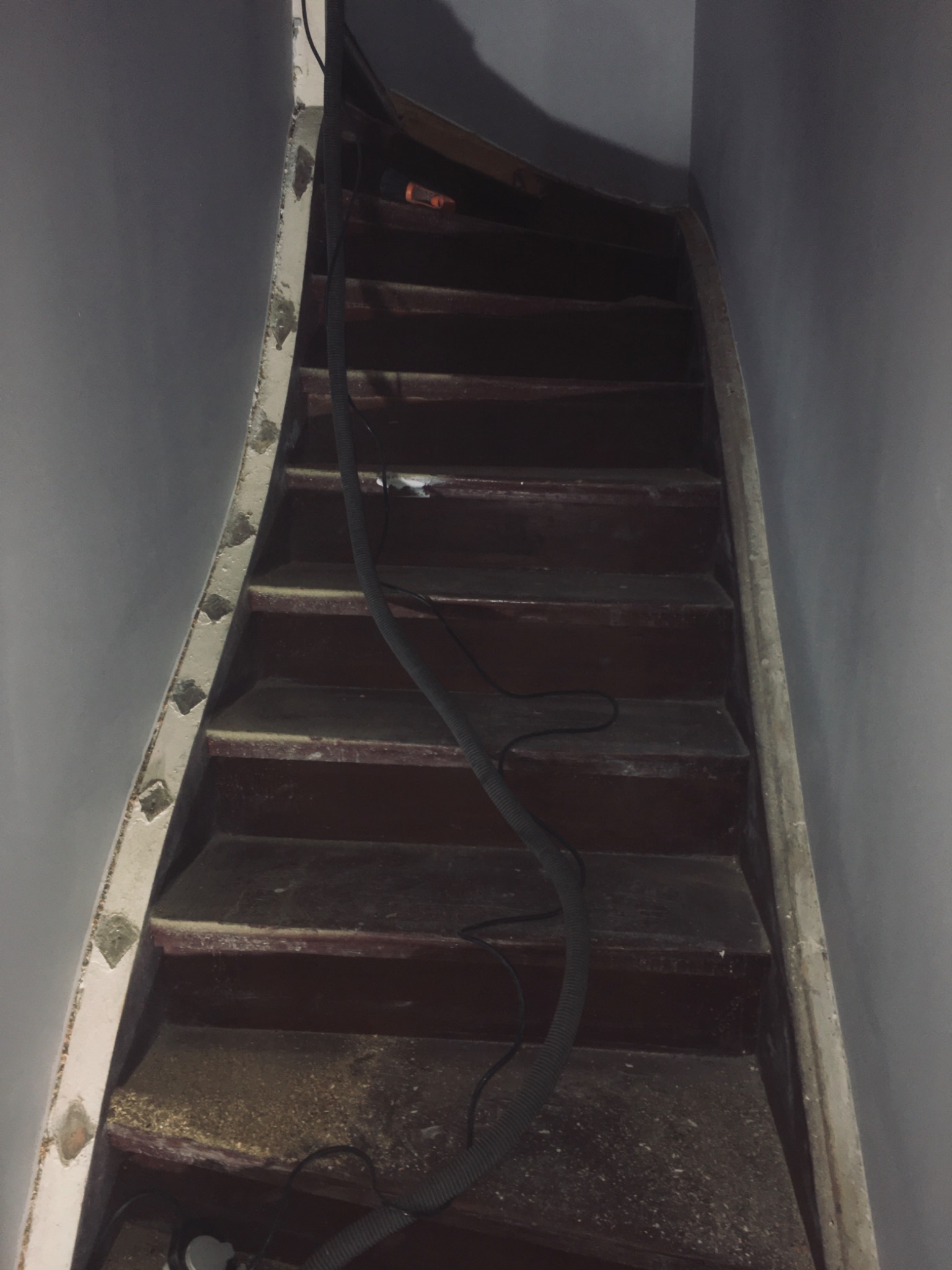 Schody drewniane w trakcie renowacji, widoczny pył i wąż od odkurzacza, ślady szpachli na listwie bocznej.