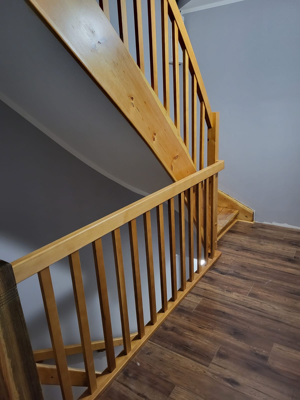 Drewniane schody z balustradą z pionowych szczebli, widoczne z góry, z podłogą wykończoną panelami imitującymi drewno.
