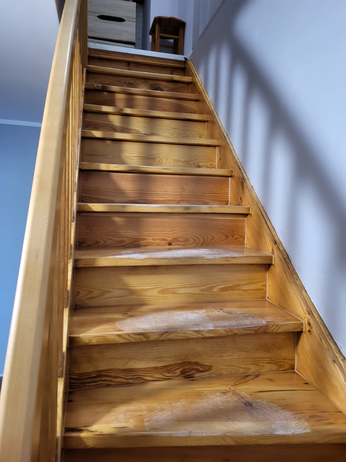 Drewniane schody w trakcie renowacji, widoczne ślady po szpachlowaniu na kilku stopniach, naturalne oświetlenie podkreśla usłojenie drewna.