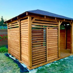 DrewLand - Drewniana konstrukcja z zadaszeniem na trawie, z elementami lamelowymi, prawdopodobnie w trakcie montażu, widoczne zabezpieczenia podłoża.