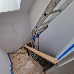 RS BUD - Przygotowania do prac malarskich na schodach: zabezpieczone folią i taśmą malarską, ustawiona aluminiowa drabina, widoczne okno dachowe.