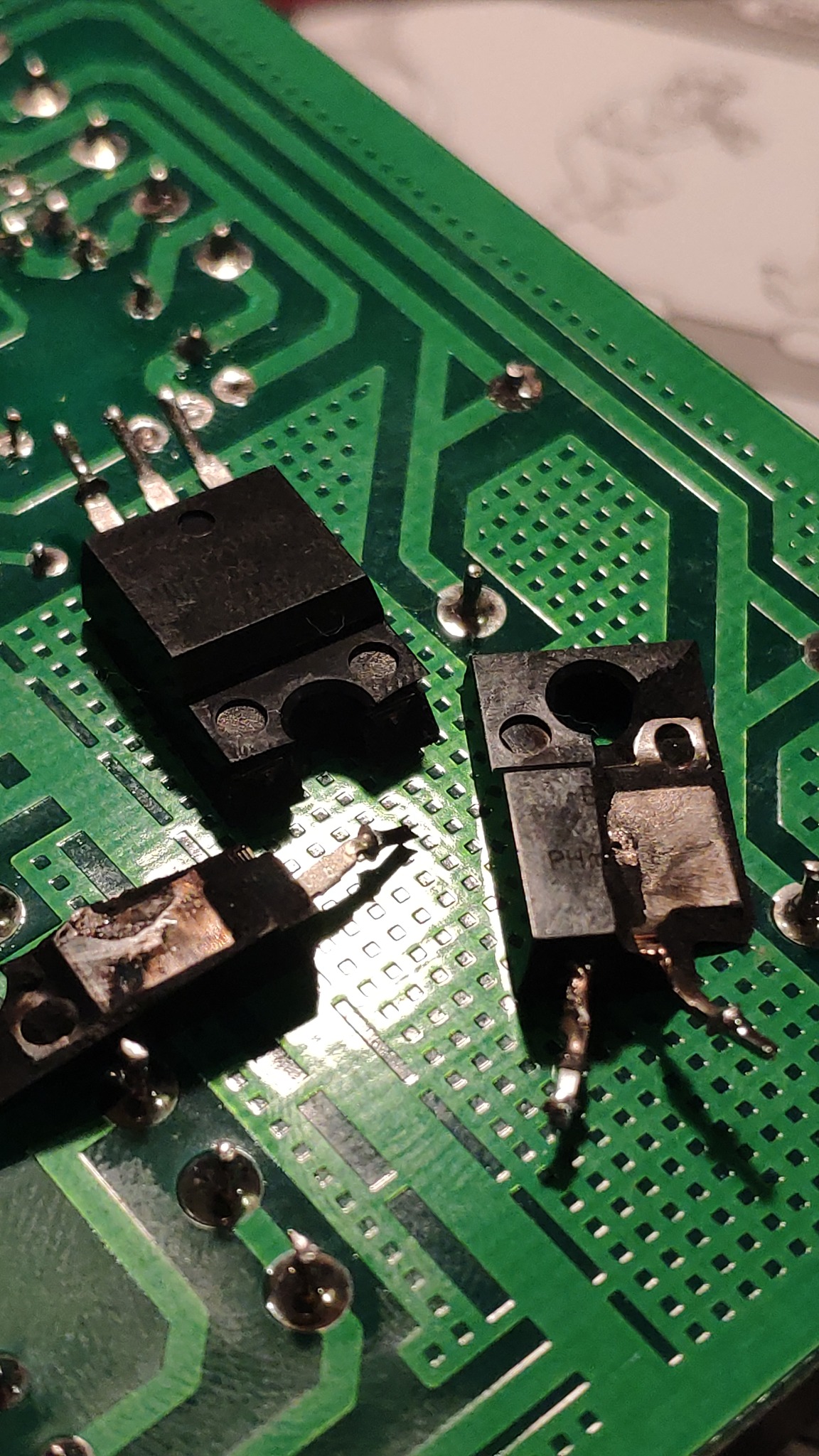 Uszkodzone elementy elektroniczne, w tym scalone układy, na zielonej płytce drukowanej z widocznymi śladami przepalenia.