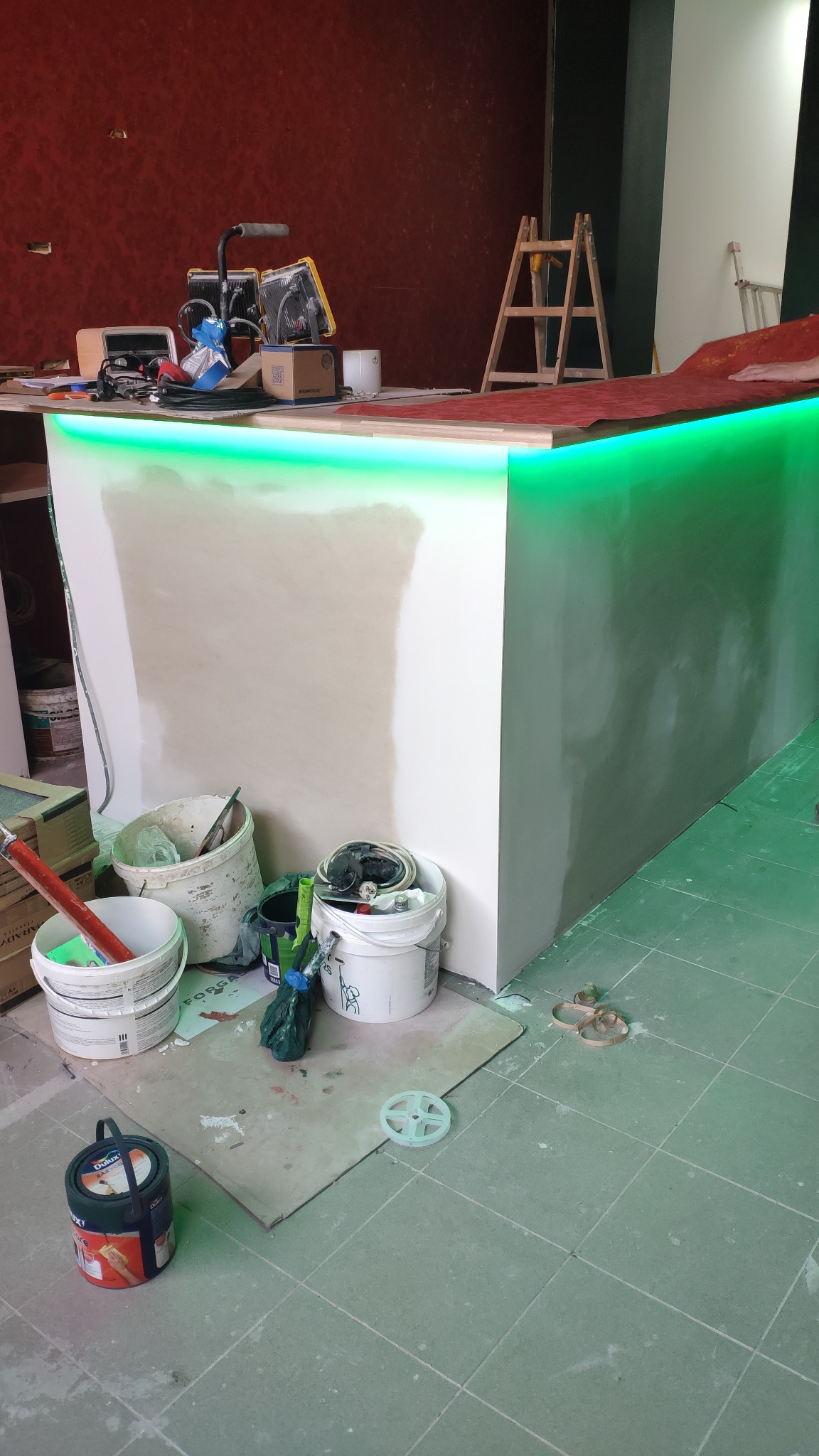 Bar w trakcie wykańczania z podświetleniem LED, widoczne narzędzia i materiały budowlane, drabina w tle.