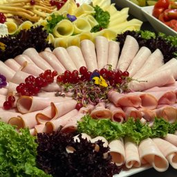 Olszańska Gastro Concept - Dekoracyjna taca z wędlinami, serami, sałatą i owocami, idealna na catering świąteczny lub firmowy. Centralny punkt stołu, bogata kompozycja.