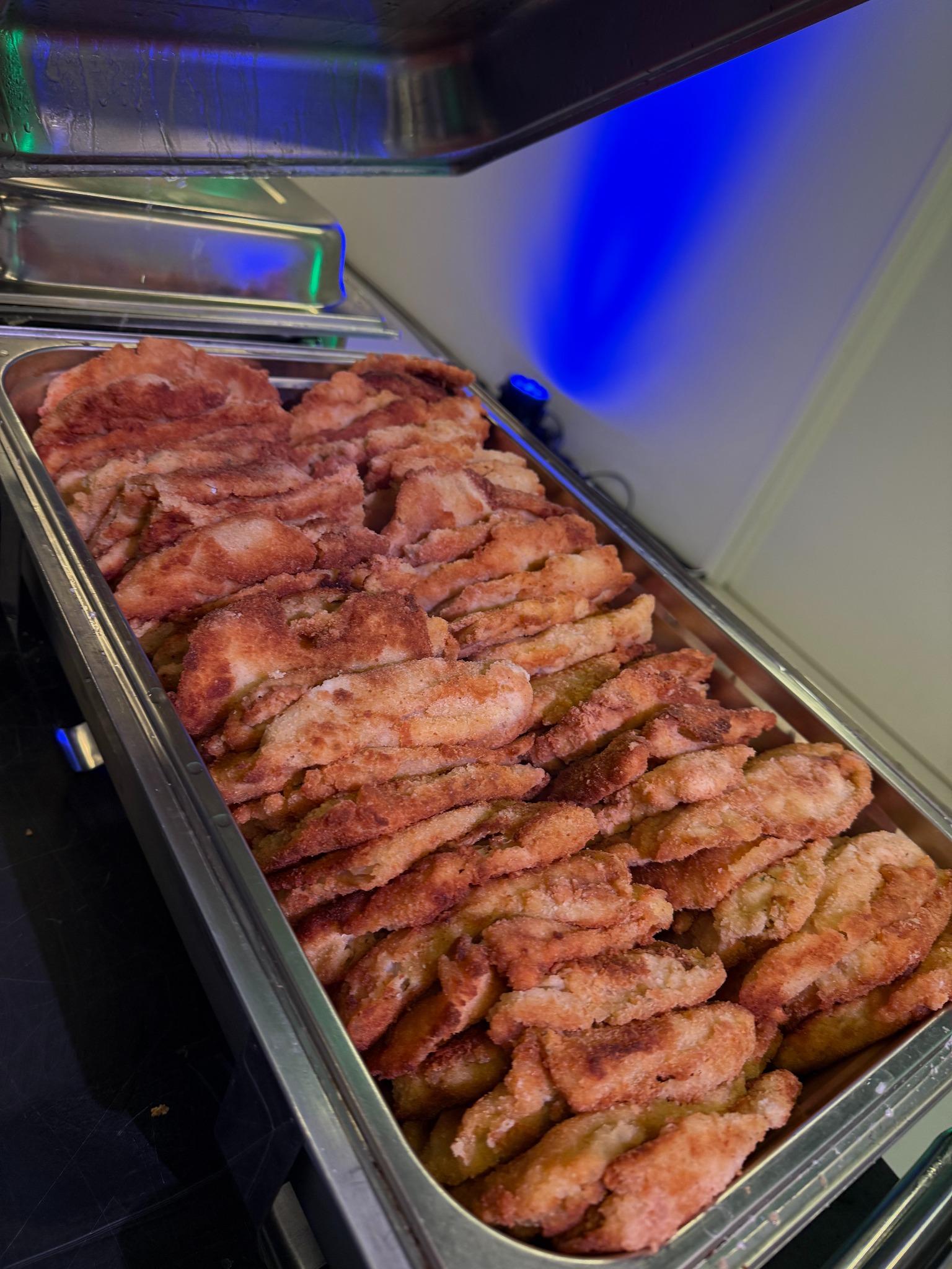 Metalowa taca wypełniona smażonymi kotletami w panierce, oświetlona niebieskim światłem. Potrawa gotowa do serwowania, idealna na catering firmowy lub świąteczny.