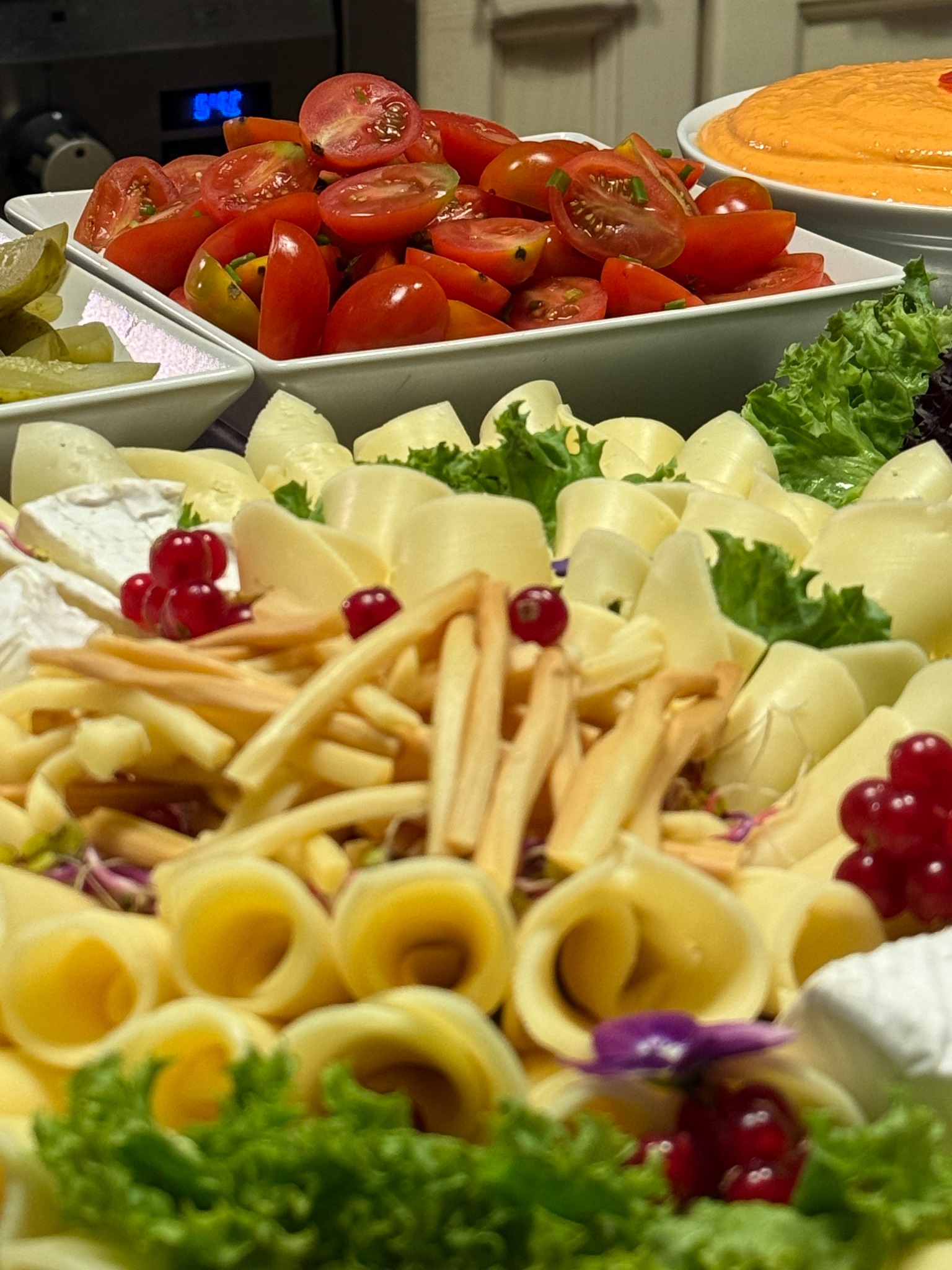 Bogato zdobiona deska serów i przekąsek z pomidorkami koktajlowymi, roladkami serowymi, brie i czerwonymi porzeczkami, idealna na elegancki catering.