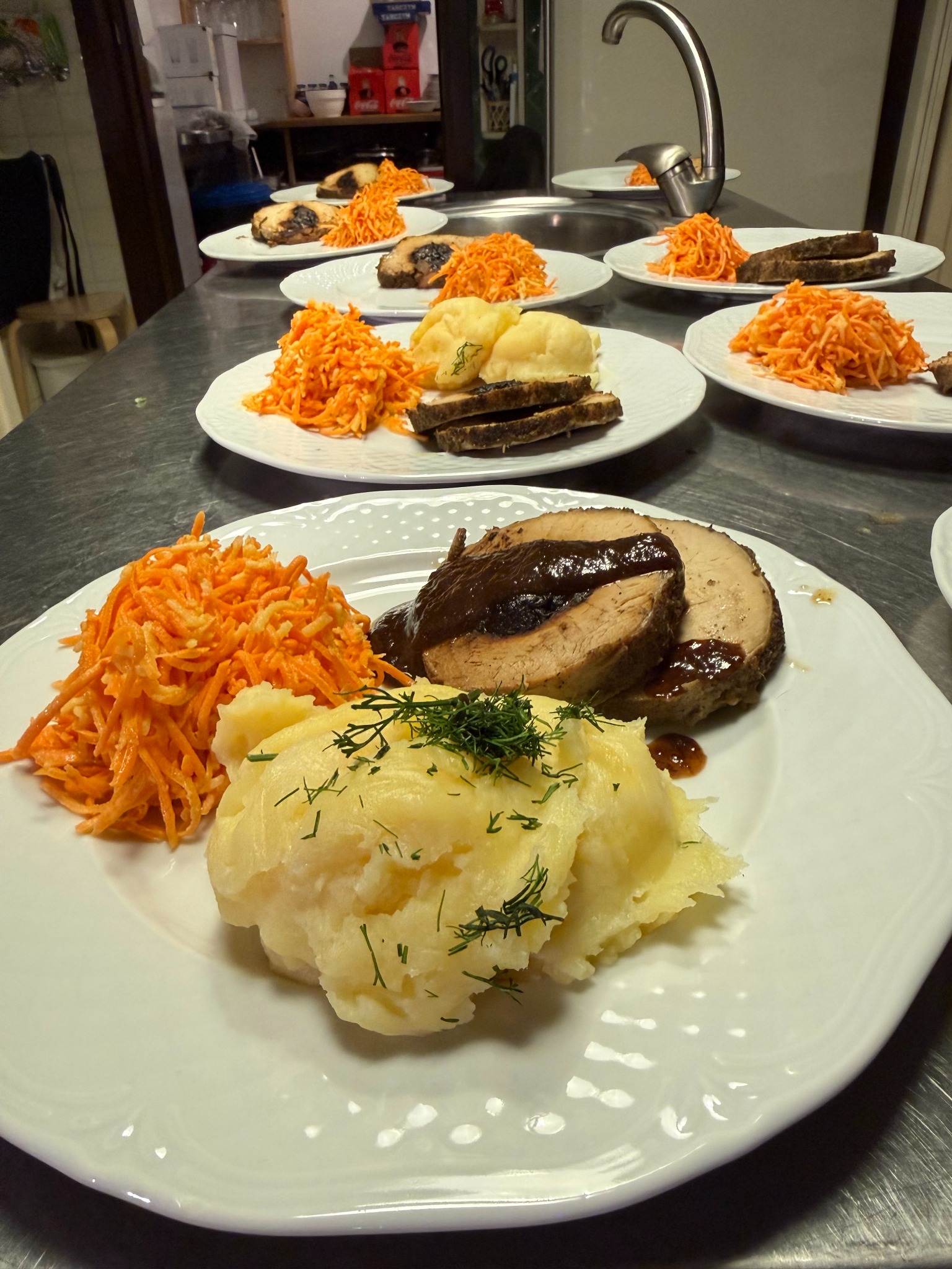 Porcje obiadowe na białych talerzach: mięso w sosie, puree ziemniaczane z koperkiem i surówka z marchewki. Przygotowane do wydania, widok z góry.