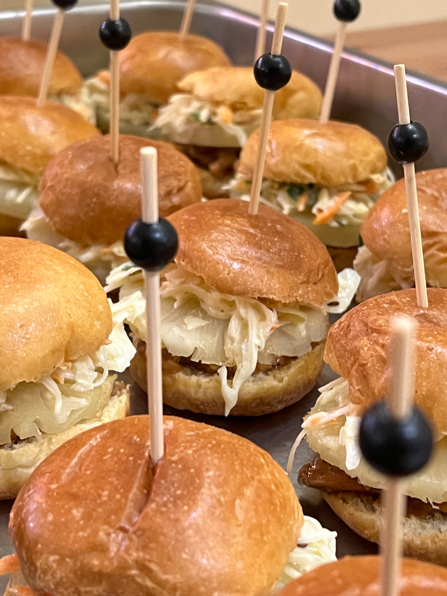 Apetyczne mini burgery z jasną kapustą i dekoracyjnymi wykałaczkami na metalowej tacy, gotowe do serwowania na przyjęciu.