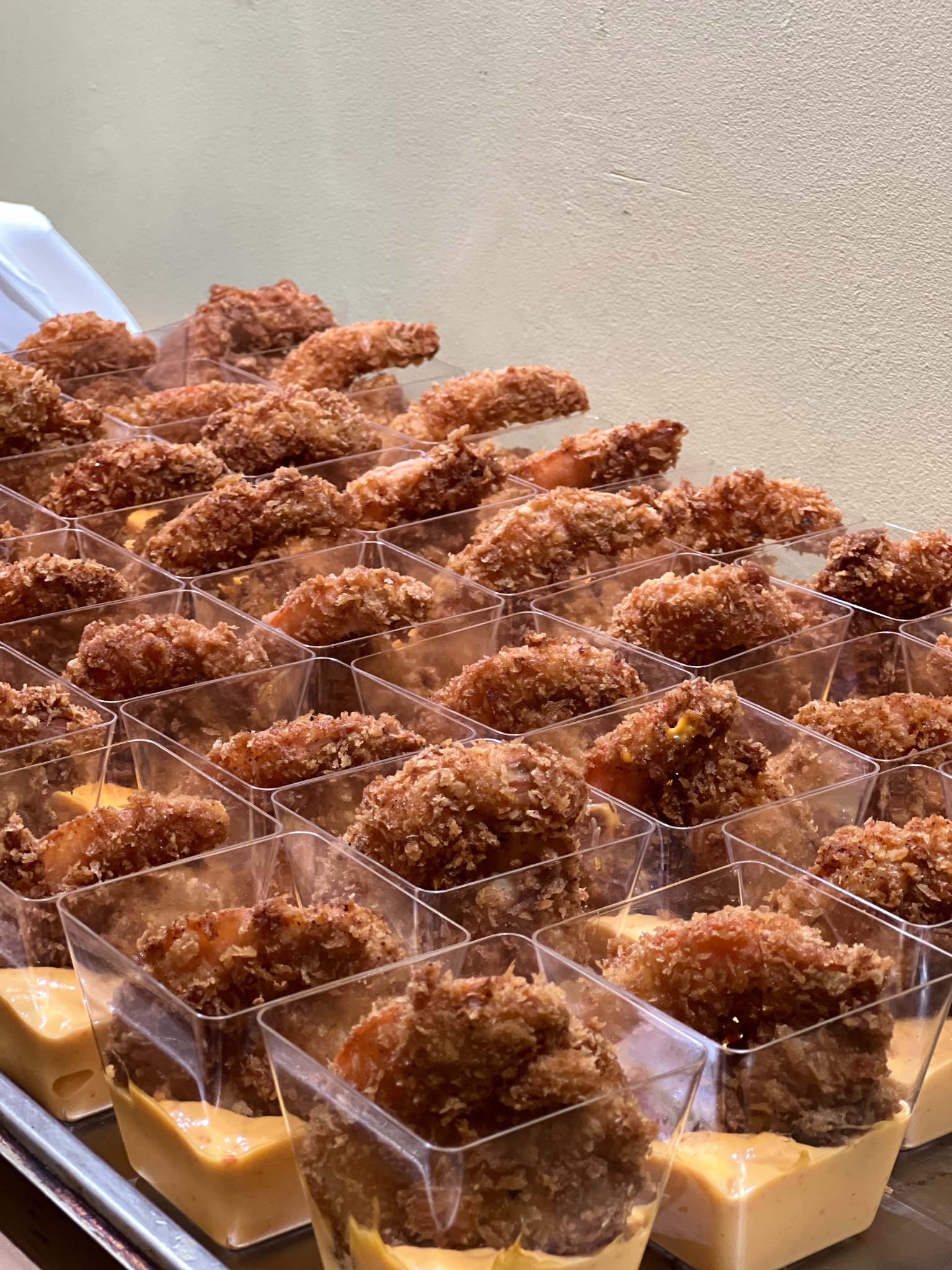 Rzędy apetycznych przekąsek cateringowych: smażone krewetki w panierce, podane w przezroczystych pojemnikach z kremowym sosem. Idealne na eleganckie przyjęcie.