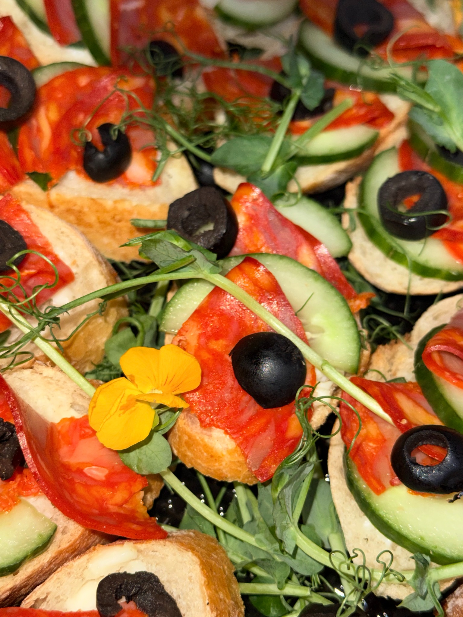 Dekoracyjne kanapeczki z salami, ogórkiem, oliwkami i jadalnymi kwiatami, ułożone blisko siebie. Idealne na catering imprezowy, widok z góry.