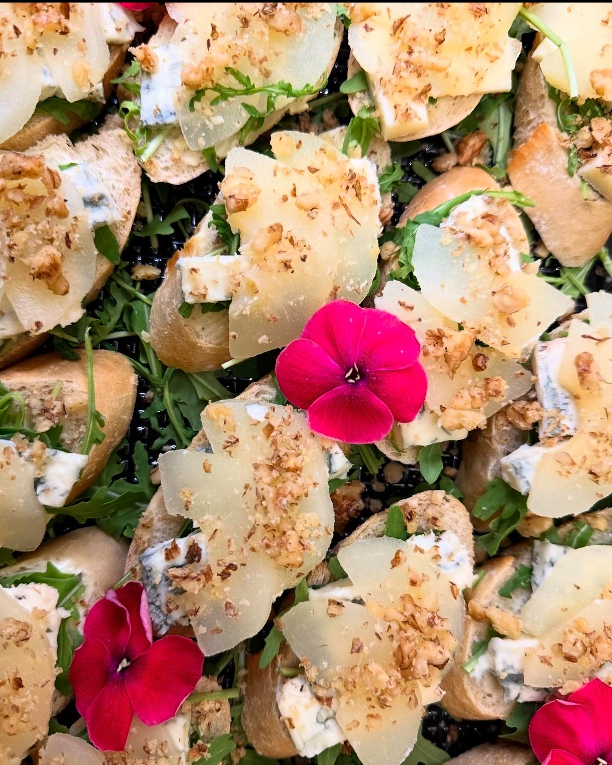 Wykwintne kanapeczki z serem pleśniowym, gruszką, orzechami i rukolą, udekorowane jadalnymi kwiatami. Elegancki catering na przyjęcie.