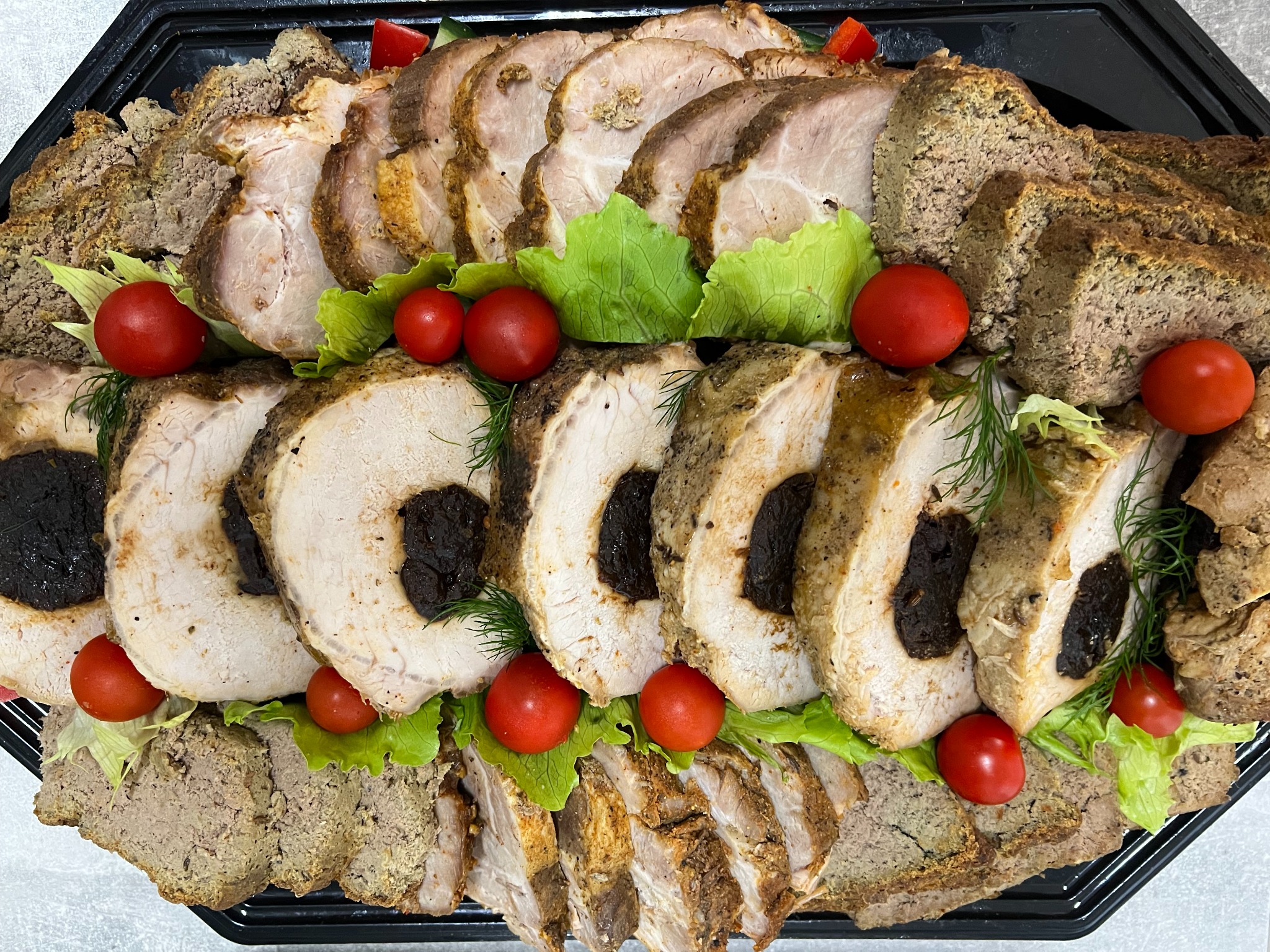 Elegancka taca z plastrami pieczonego mięsa nadziewanego śliwkami, pasztetu, pomidorków cherry i sałaty, tworząca apetyczną kompozycję.