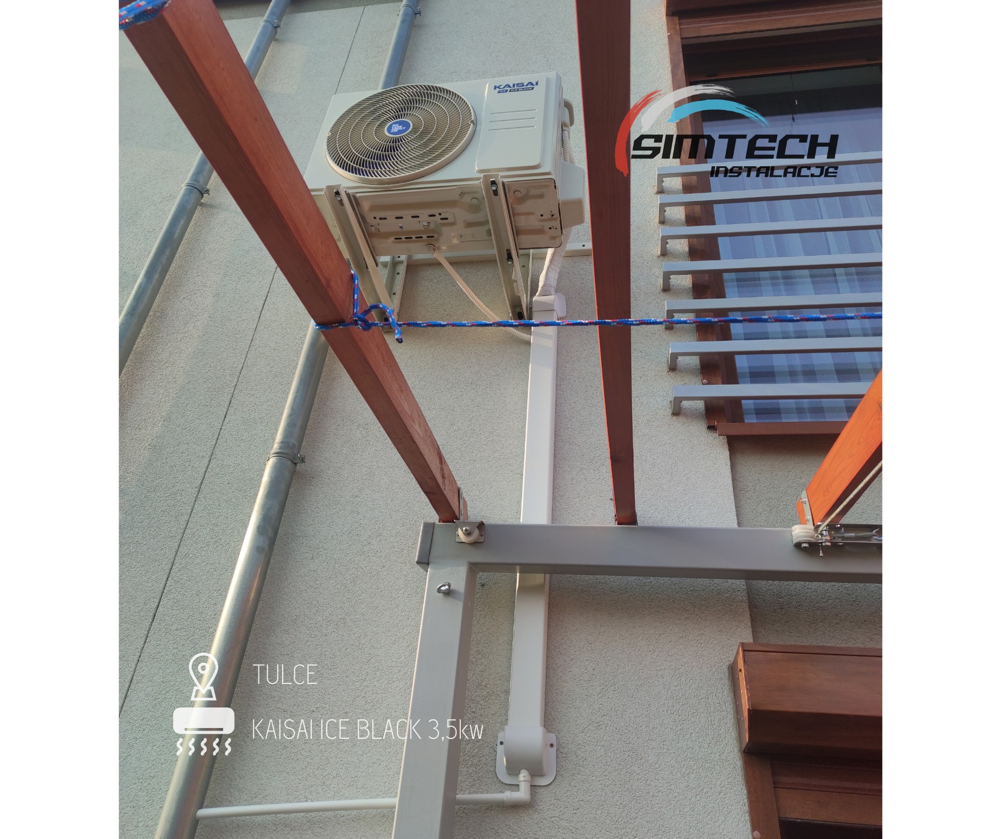 Zewnętrzna jednostka klimatyzatora Kaisai Ice Black 3.5kW zamontowana na ścianie budynku, zabezpieczona liną na czas montażu pergoli.