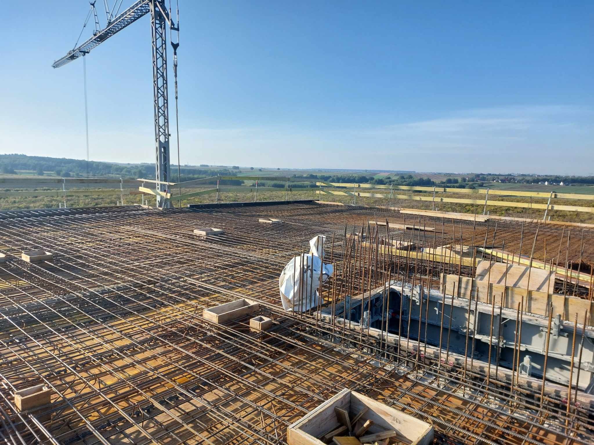 Zbrojenie płyty fundamentowej domu jednorodzinnego z widocznym dźwigiem budowlanym i elementami szalunków.