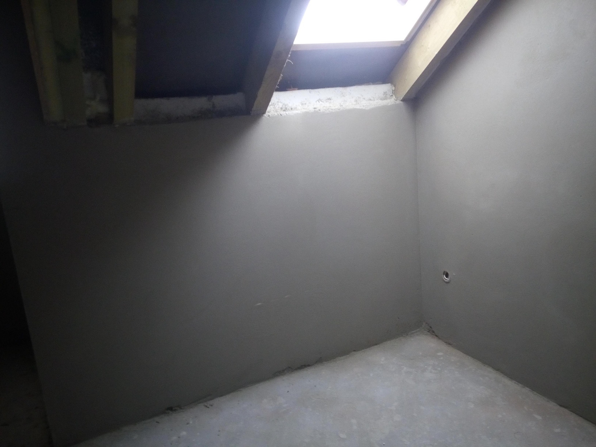 Wnętrze pomieszczenia po nałożeniu gładzi szpachlowej na ściany i sufit, widoczne drewniane elementy konstrukcyjne w górnej części kadru oraz otwór wentylacyjny w ścianie.