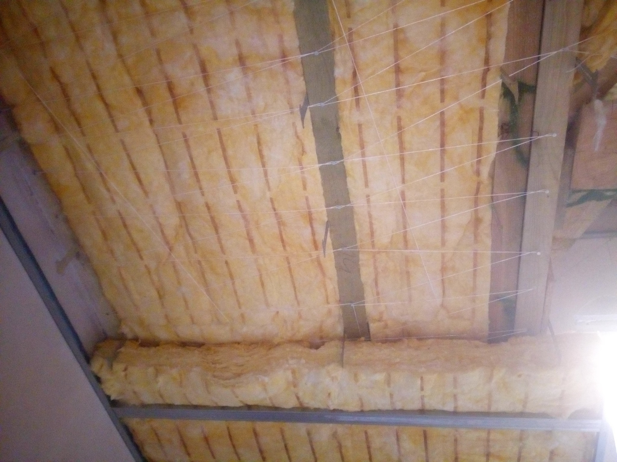 Izolacja stropu wełną mineralną, zabezpieczona sznurkiem, widoczne elementy konstrukcji drewnianej i metalowej.