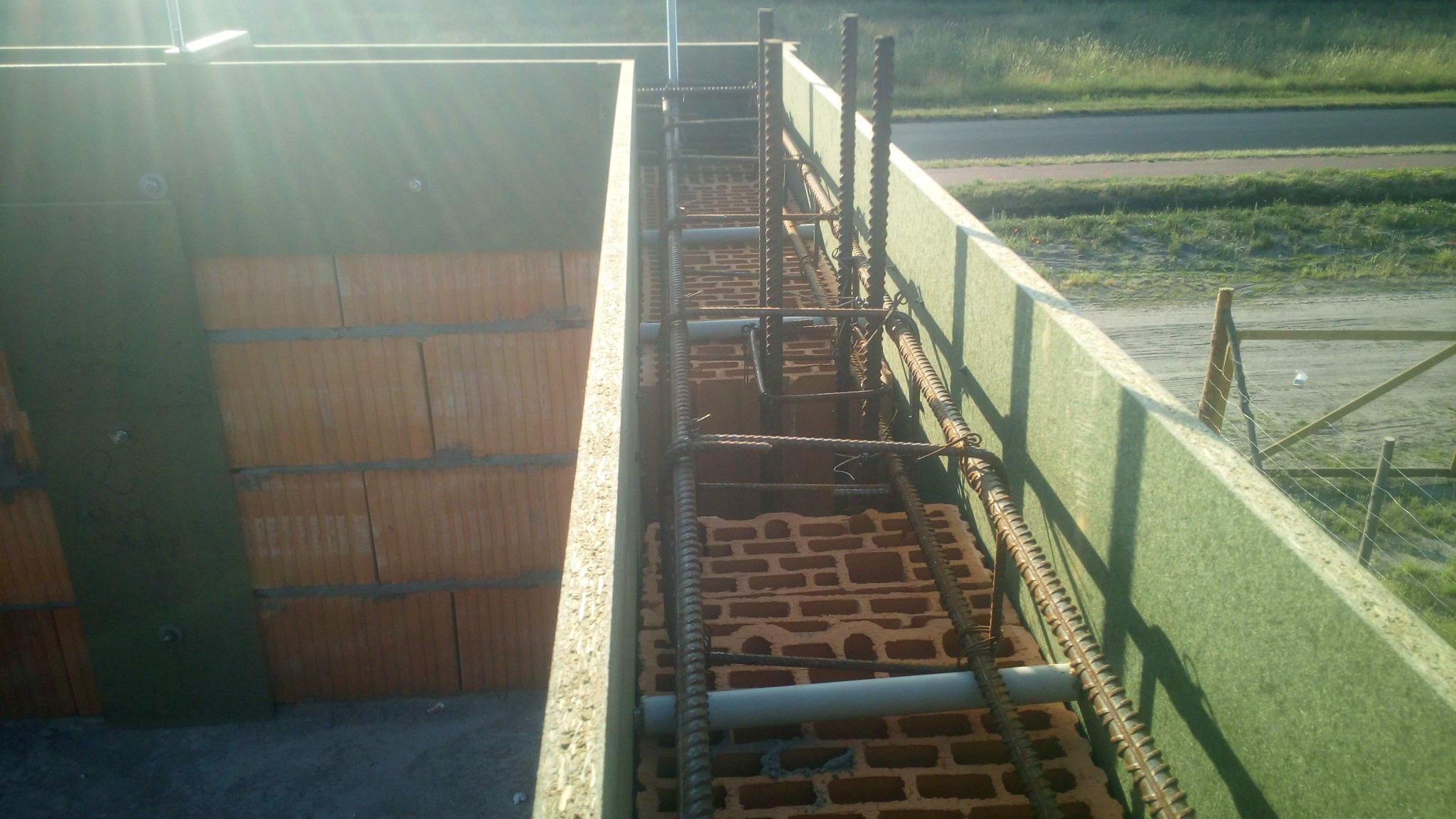 Zbrojenie fundamentów z użyciem cegieł szamotowych i stalowych prętów, zabezpieczone zieloną izolacją pionową, widok z góry na plac budowy.