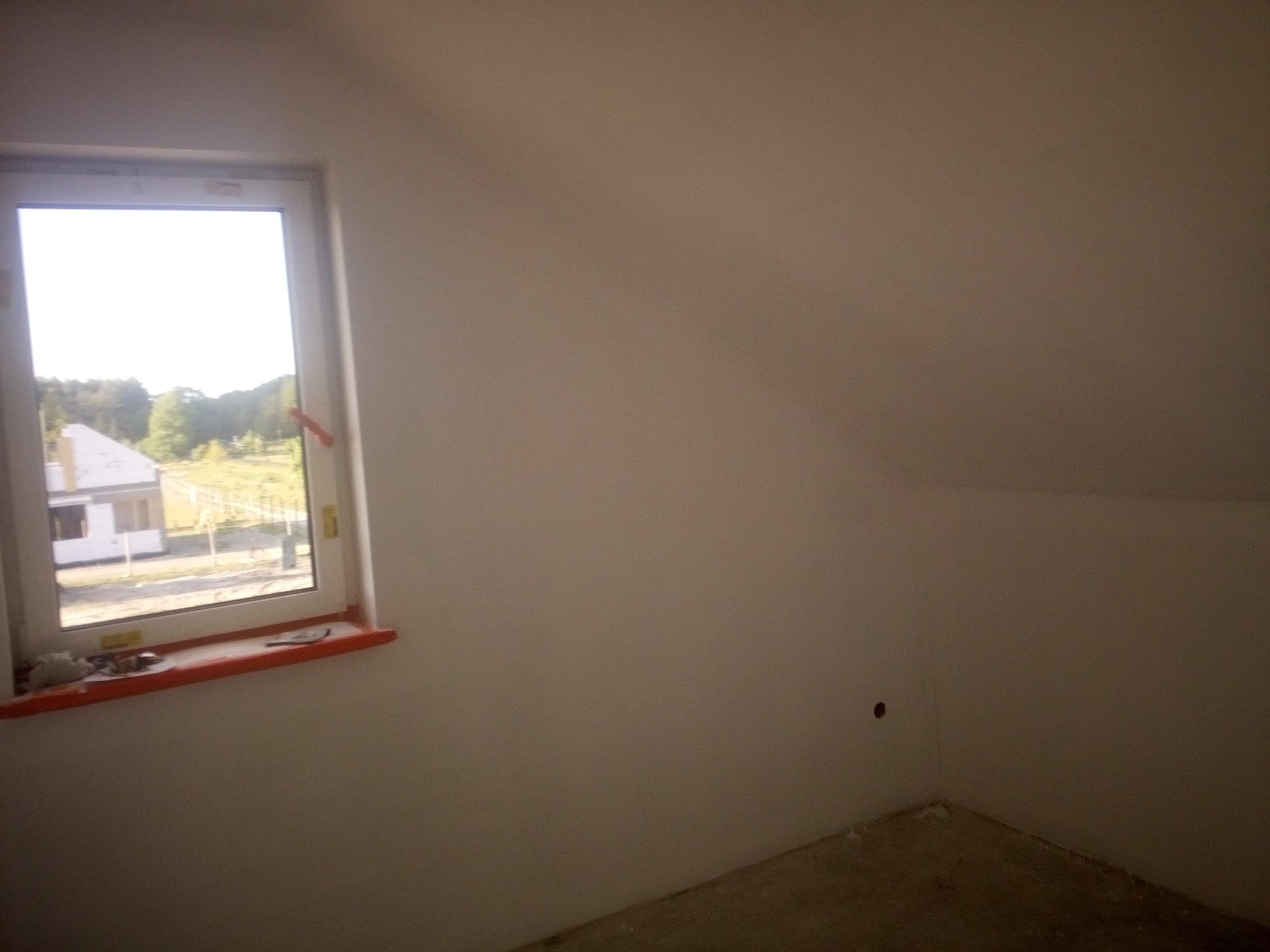 Pokój na poddaszu po malowaniu ścian na jasny kolor, widoczne okno z parapetem na którym leżą drobne narzędzia i resztki materiałów malarskich. Na ścianie widoczny mały otwór.