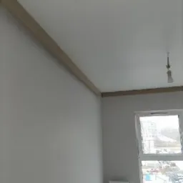 Świeżo pomalowane wnętrze pokoju z widoczną listwą przypodłogową, grzejnikiem pod oknem i gołą żarówką zwisającą z sufitu.