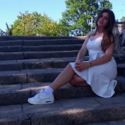 Kobieta w letniej sukience siedzi na kamiennych schodach w parku.