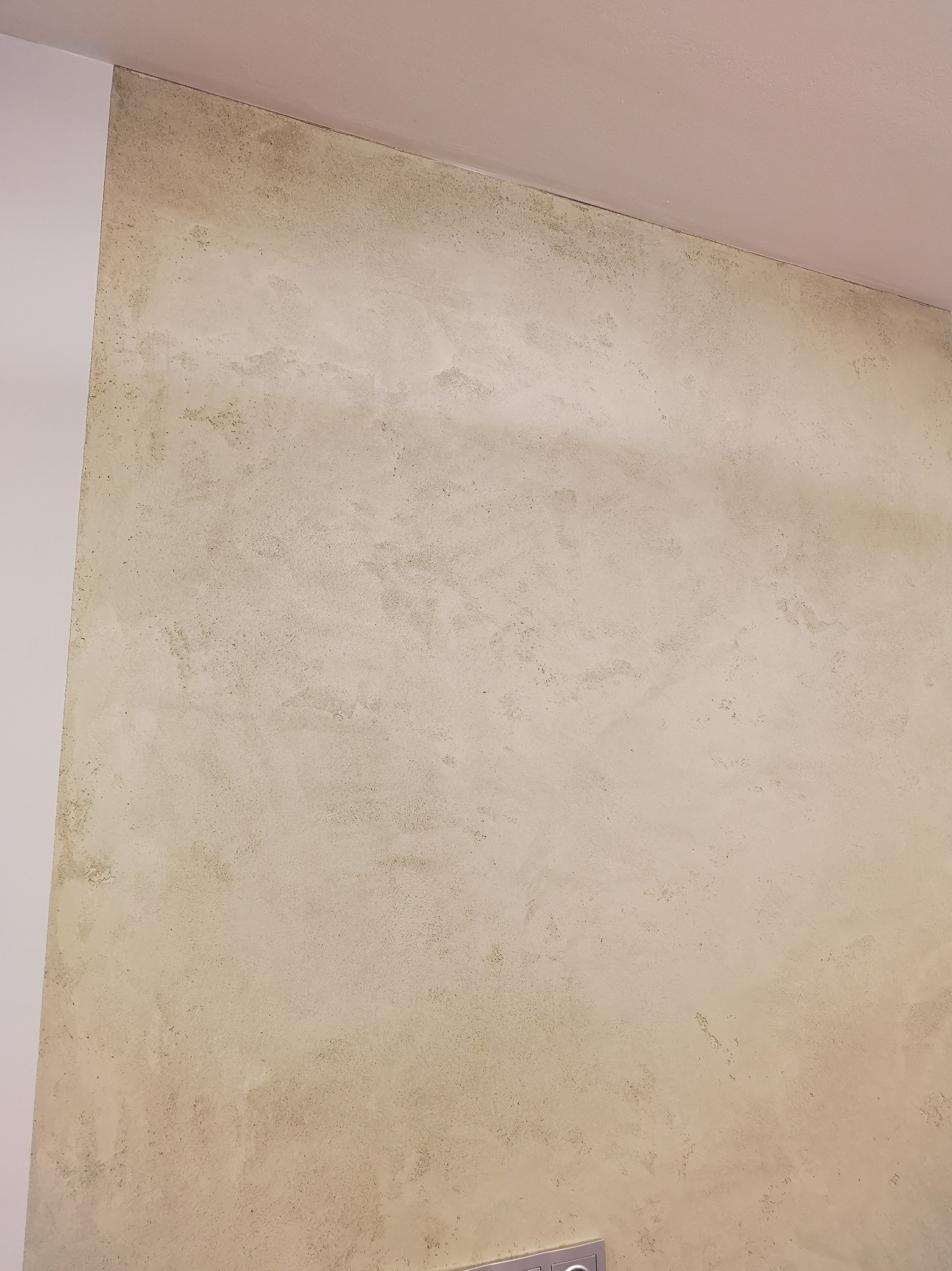 Ściana z efektem betonu architektonicznego w odcieniach beżu i szarości, widoczne nieregularne wzory i faktura, narożnik ściany pomalowany na biało.