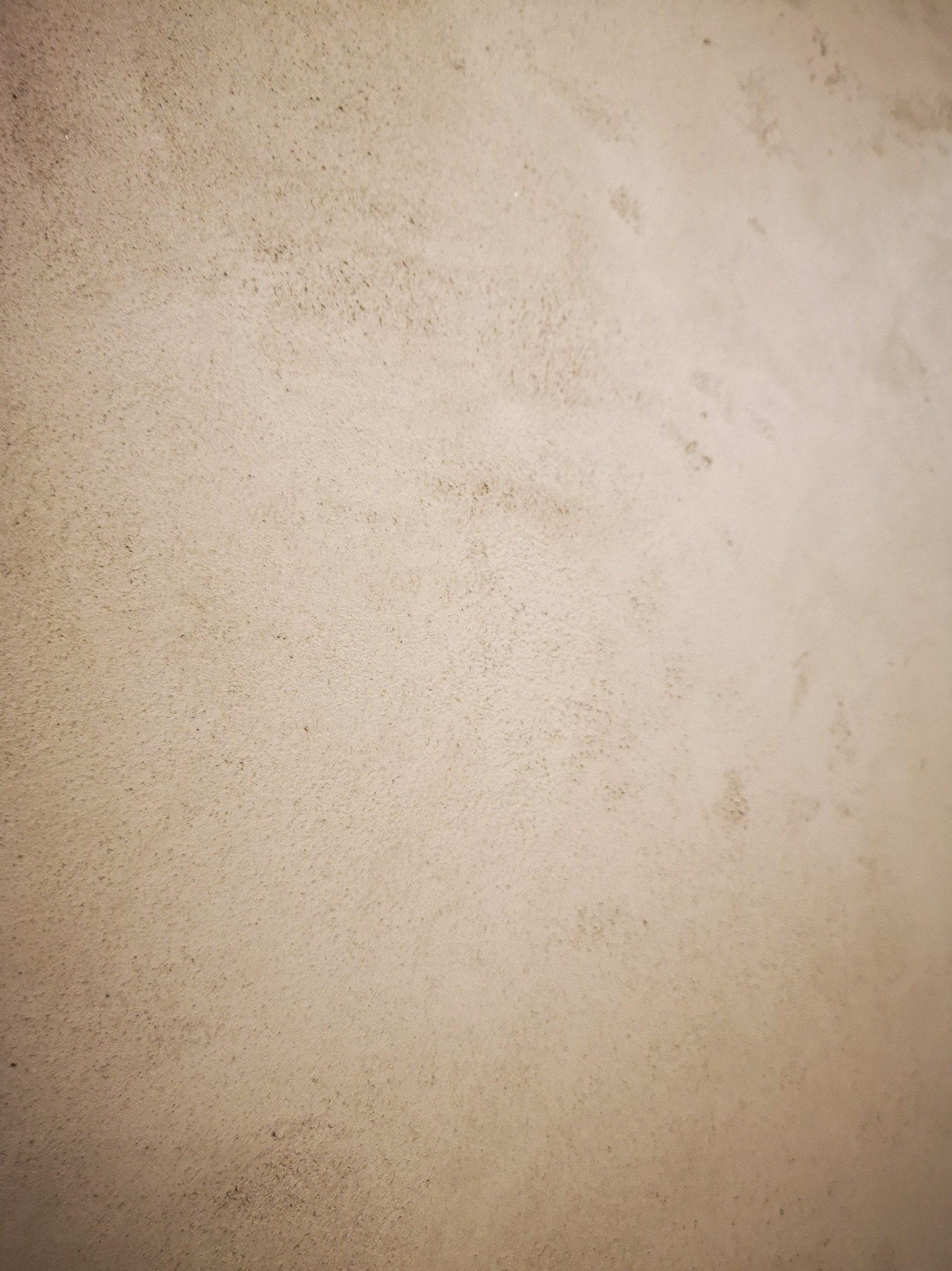 Szara ściana z widoczną strukturą, prawdopodobnie po nałożeniu gładzi, z drobnymi nierównościami i delikatnym cieniowaniem.