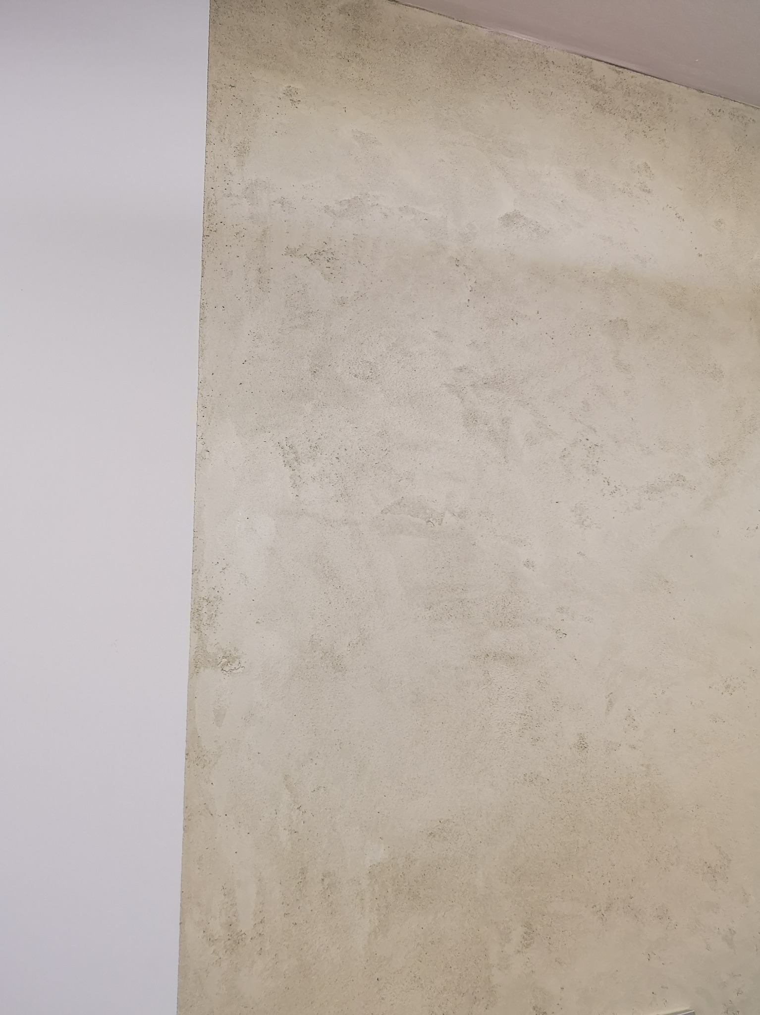 Fragment ściany z dekoracyjną fakturą w odcieniach beżu, sąsiadującej z gładką, białą ścianą. Widoczny narożnik pomieszczenia.