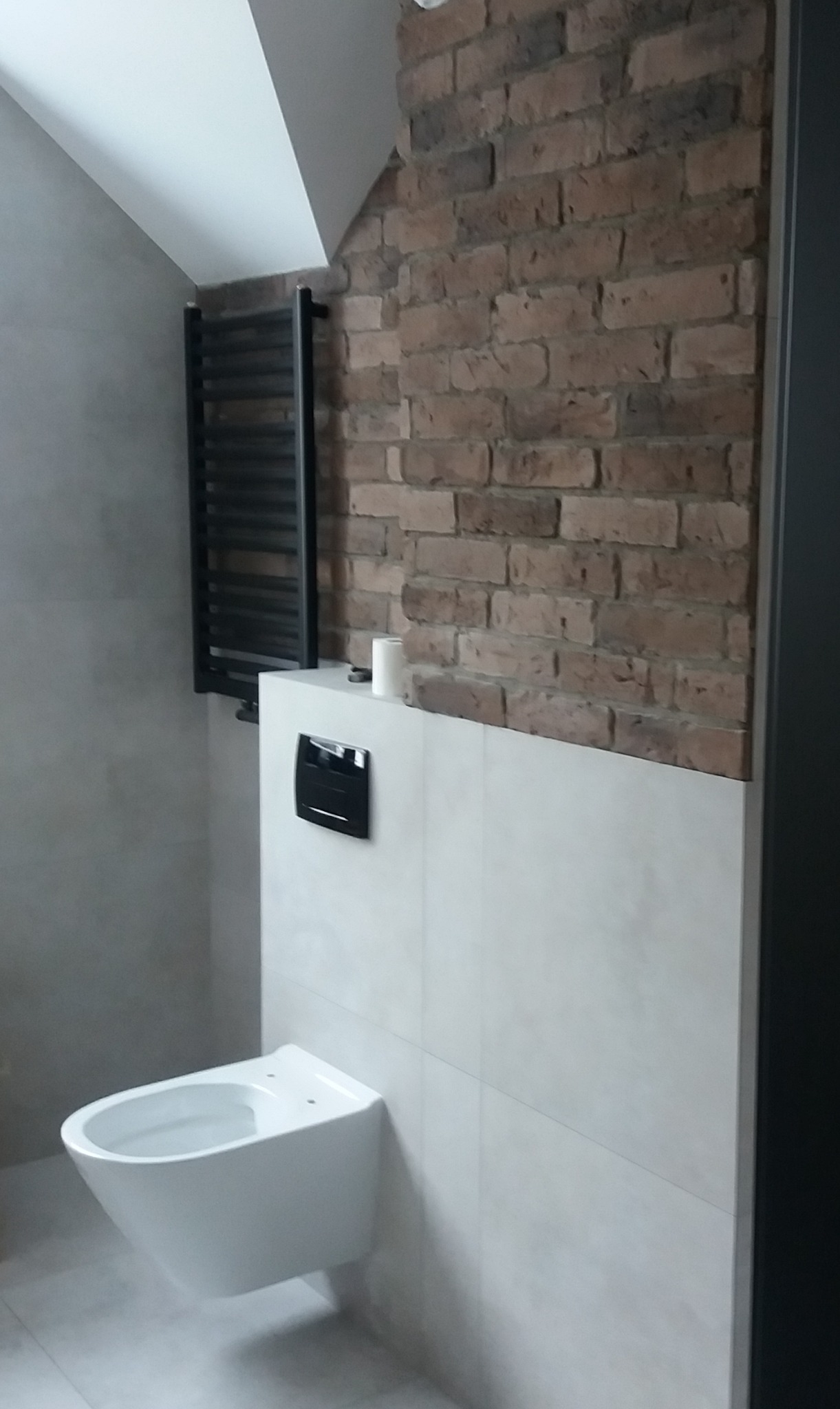 Nowoczesna łazienka z wiszącą toaletą, grzejnikiem drabinkowym i ścianą z cegły dekoracyjnej w odcieniach brązu i szarości.