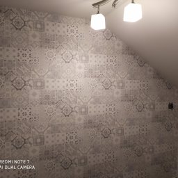 Usługi Ogólnobudowlane Michał Ruszyński - Ściana w łazience wyłożona ozdobnymi, szarymi płytkami w stylu patchwork, oświetlona lampą sufitową.