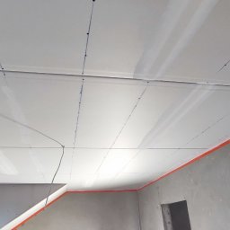 Usługi Ogólnobudowlane Michał Ruszyński - Montaż płyt gipsowo-kartonowych na suficie, widoczne linie wyznaczające punkty mocowania, zabezpieczone pomarańczową taśmą krawędzie ścian.