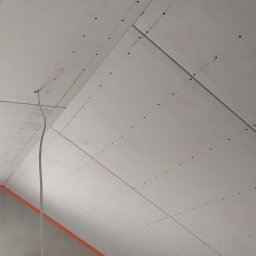 Usługi Ogólnobudowlane Michał Ruszyński - Poddasze z zamontowanymi płytami gipsowo-kartonowymi, widoczne ślady po szpachlowaniu i widoczny przewód elektryczny, przygotowane do dalszych prac wykończeniowych.