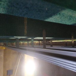 Usługi Ogólnobudowlane Michał Ruszyński - Poddasze w trakcie ocieplania: widoczne metalowe profile mocujące izolację, żółta wełna mineralna oraz konstrukcja dachu. Silne światło w dolnej części kadru.