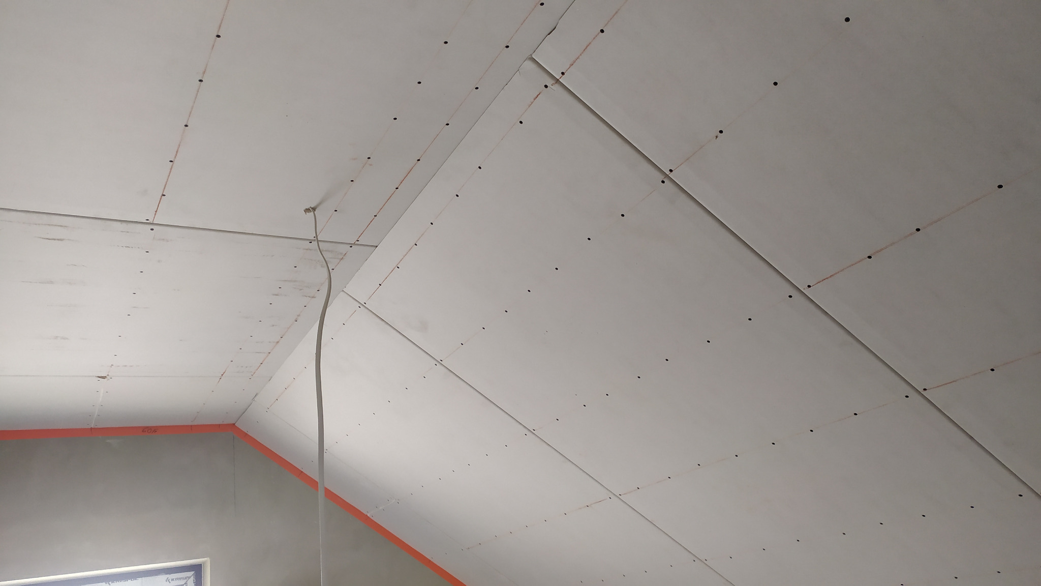 Poddasze z zamontowanymi płytami gipsowo-kartonowymi, widoczne ślady po szpachlowaniu i widoczny przewód elektryczny, przygotowane do dalszych prac wykończeniowych.