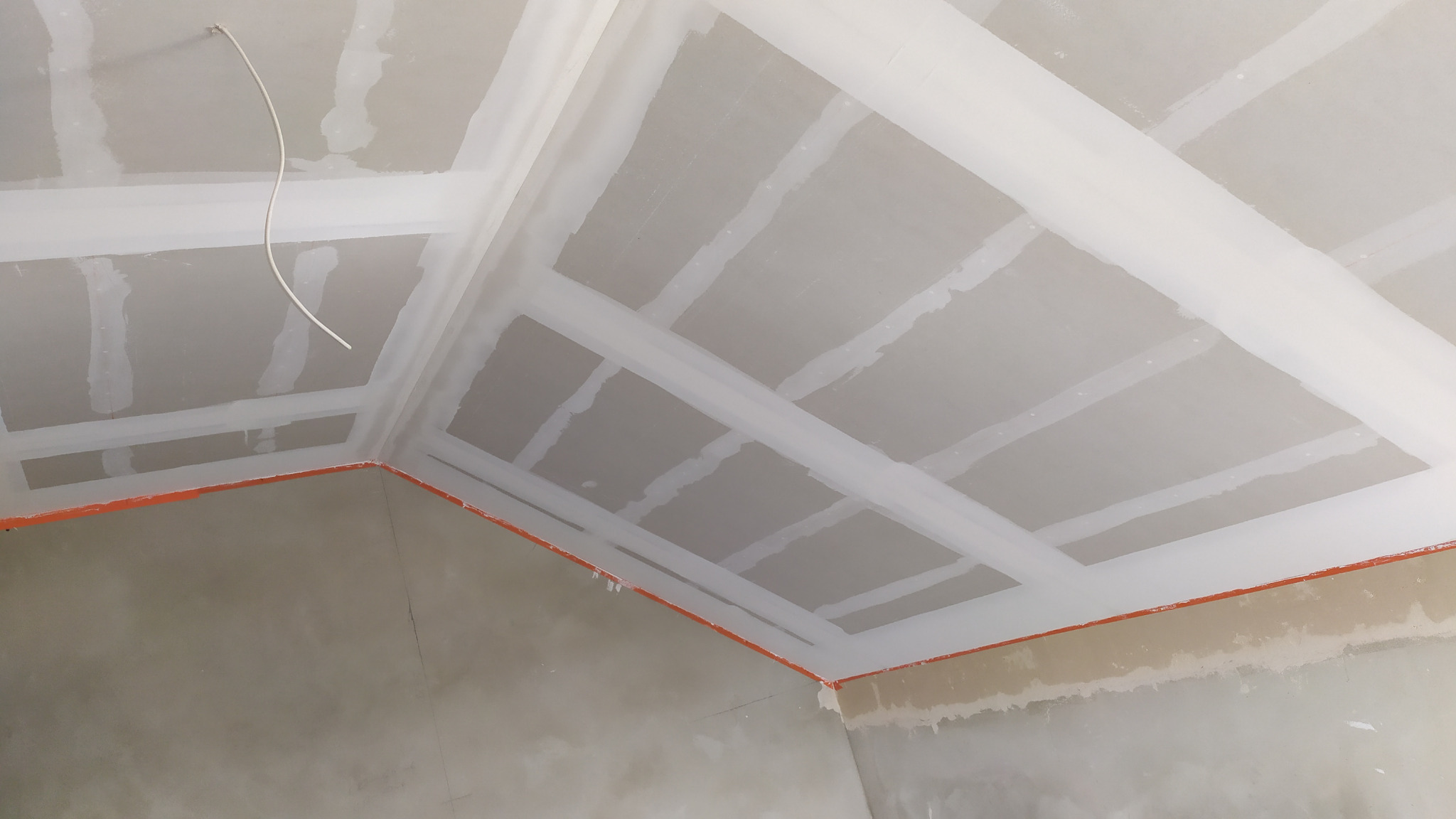 Poddasze z zamontowanymi płytami gipsowo-kartonowymi, wzmocnione konstrukcją z profili, z widocznymi łączeniami płyt przygotowanymi do szpachlowania i wystającym przewodem elektrycznym.