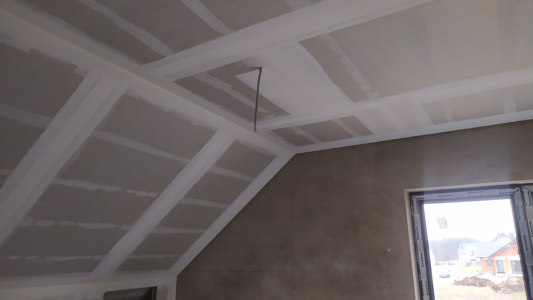 Poddasze w trakcie ocieplania w miejscowości Linia, widoczne płyty gipsowo-kartonowe na skosach dachu, szpachlowane łączenia i wystający przewód elektryczny z otworu w suficie.