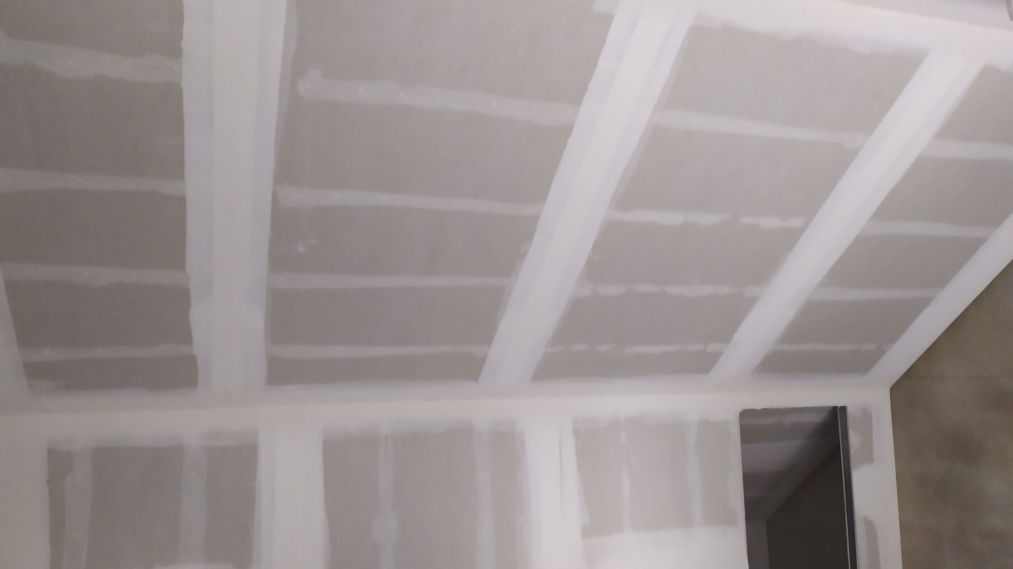 Płyty gipsowo-kartonowe zamontowane na suficie i ścianach, z widocznymi łączeniami zaszpachlowanymi na biało, przygotowane do dalszych prac wykończeniowych.