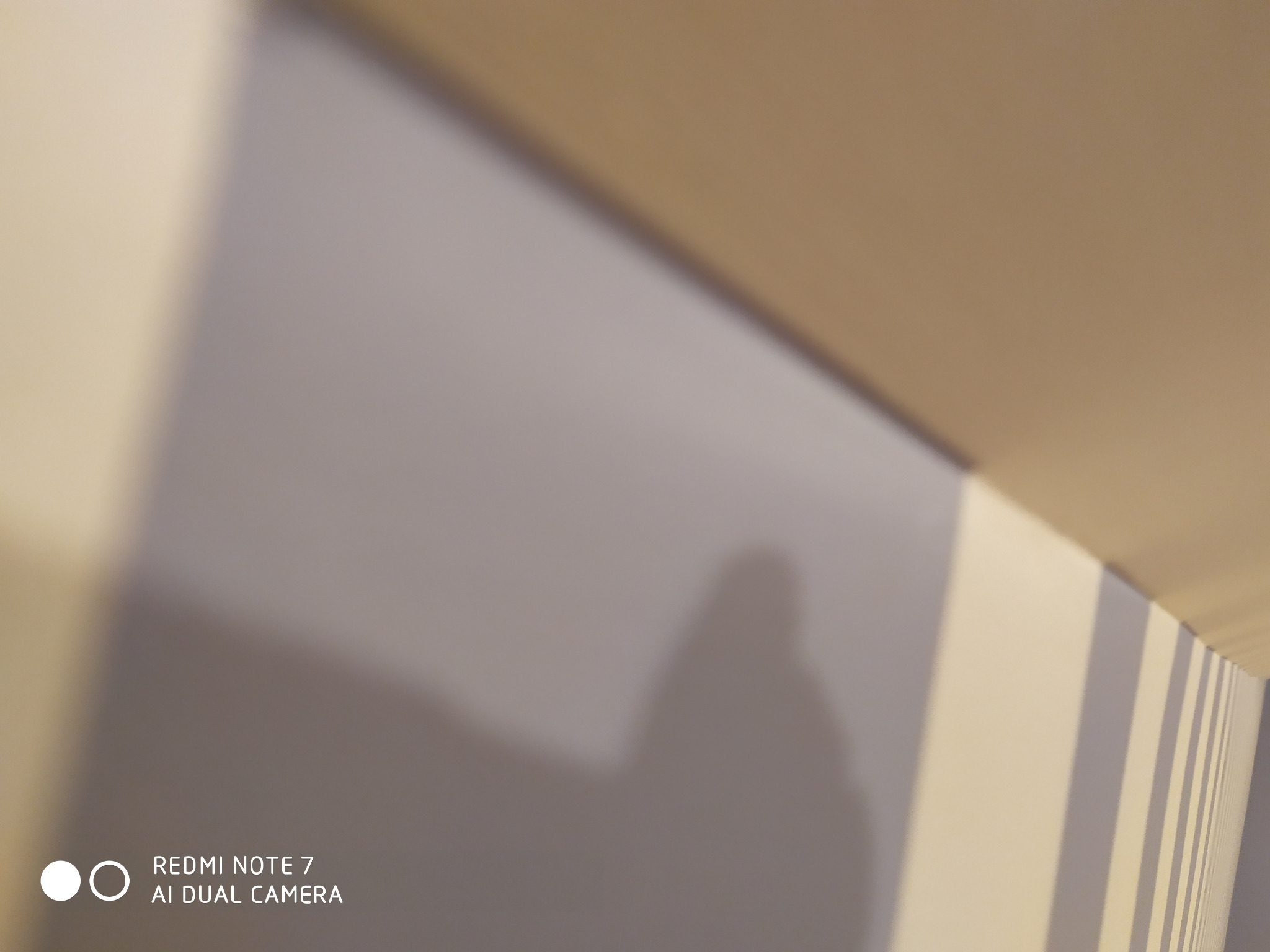 Fragment ściany pomalowanej na szaro z widocznym cieniem, z paskami w rogu pomieszczenia i logo telefonu na dole.