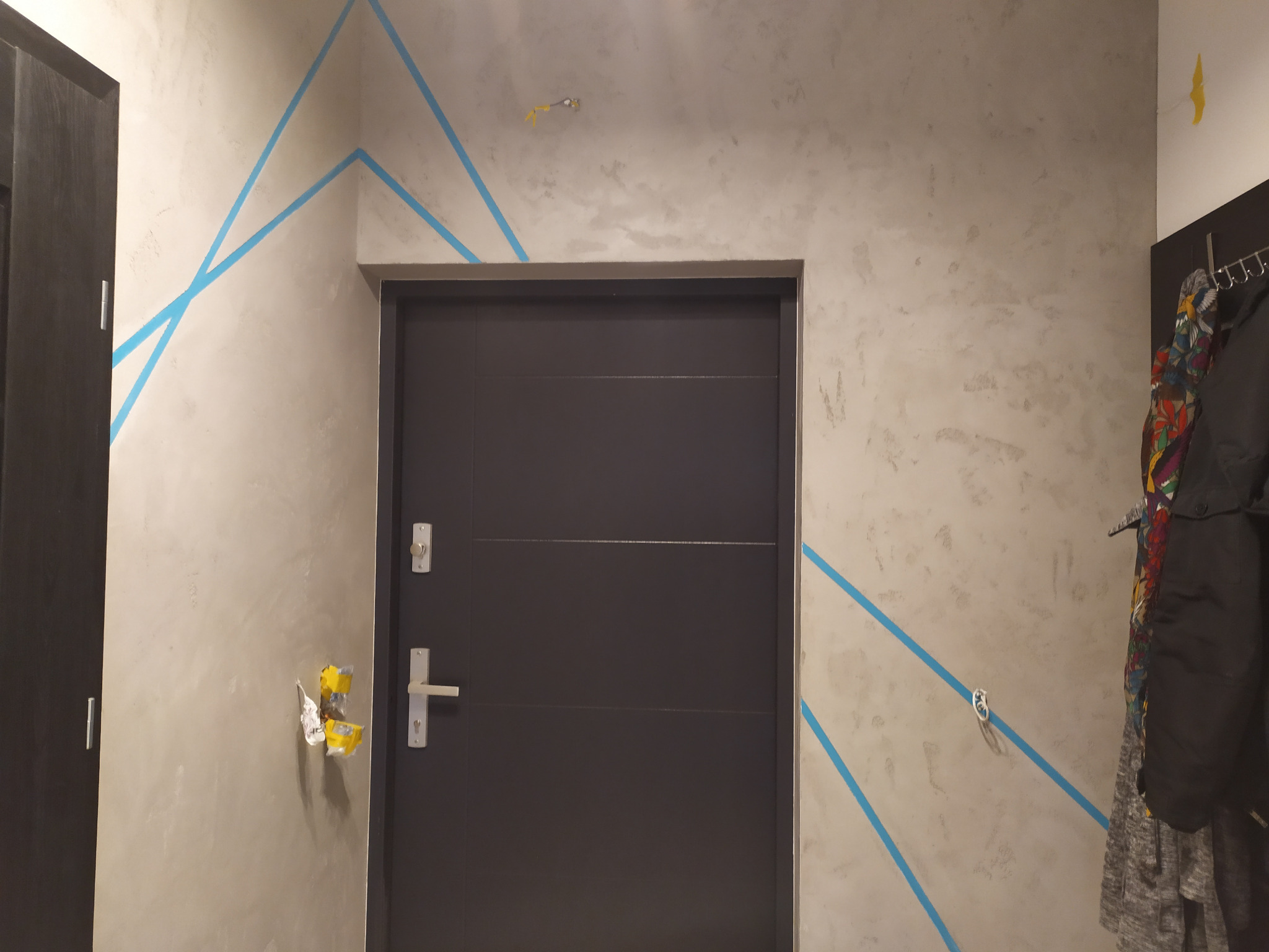 Ściana z efektem betonu architektonicznego zabezpieczona niebieską taśmą malarską przed malowaniem, widoczne gniazdko elektryczne i zamontowane drzwi.