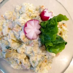 Sałatka jarzynowa w szklanej misce, udekorowana rzodkiewkami wyciętymi w kwiaty i liśćmi sałaty.