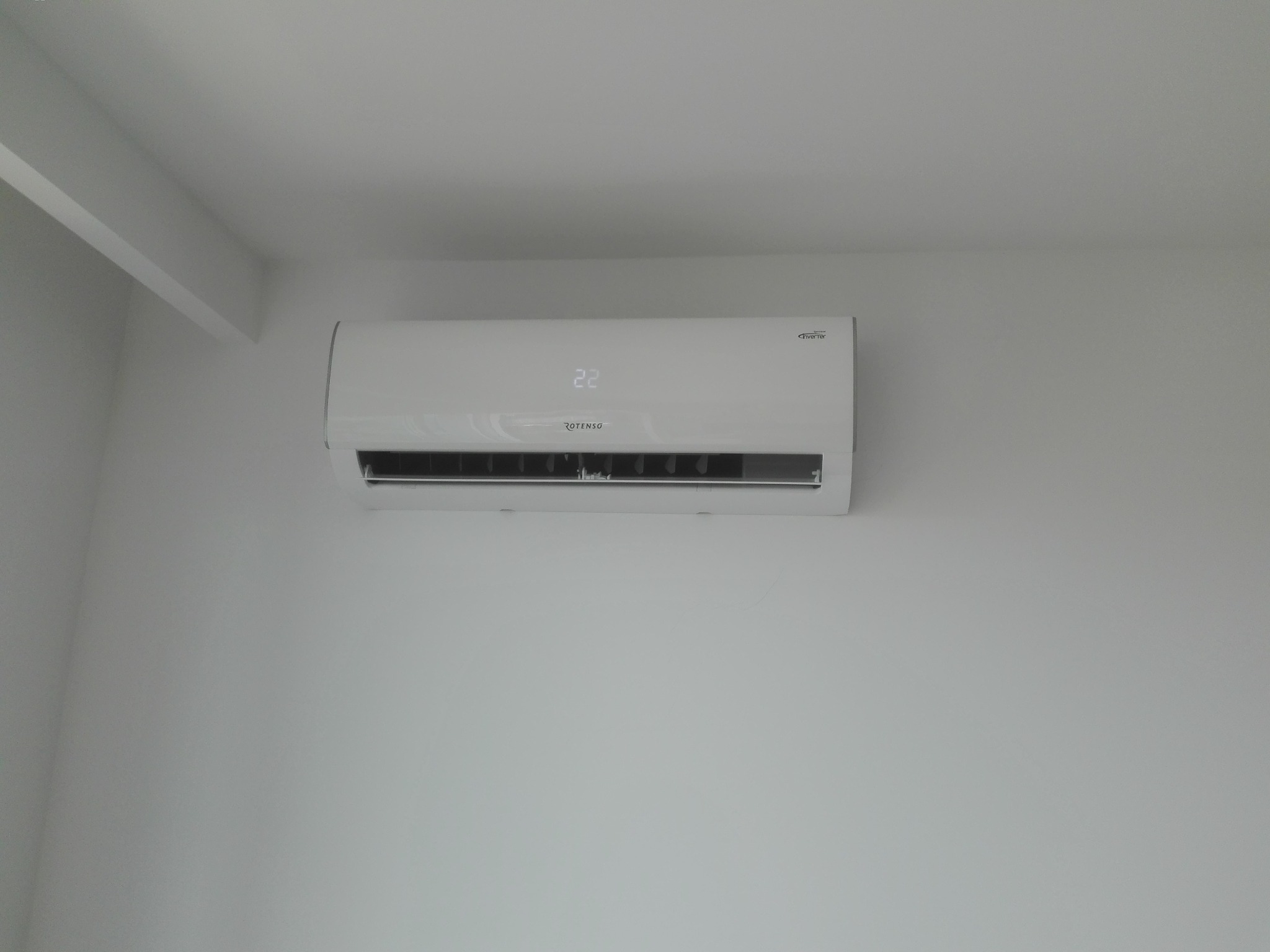 Biała, wisząca klimatyzacja Rotenso z wyświetlaczem temperatury 22 stopnie Celsjusza, zamontowana na białej ścianie w jasnym pomieszczeniu.