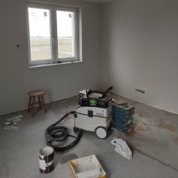 Andrzej Włodarczyk - Przygotowania do malowania ścian w nowym budynku: wiadro z farbą, kuweta z wałkiem, odkurzacz przemysłowy Festool i paczki paneli podłogowych Kronospan stoją na surowym betonowym podłożu przy...