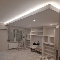 DOBRO-BUD OLEH LANOVENKO - Wnętrze w trakcie prac wykończeniowych: zabudowa z półkami, oświetlenie LED w suficie podwieszanym, drabina rozstawiona przy ścianie, widoczne narzędzia i akcesoria.