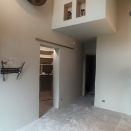 DOBRO-BUD OLEH LANOVENKO - Wnętrze po odświeżeniu ścian we Wrocławiu z widocznym pracownikiem, uchwytem na telewizor na ścianie, grzejnikiem i otwartą garderobą.