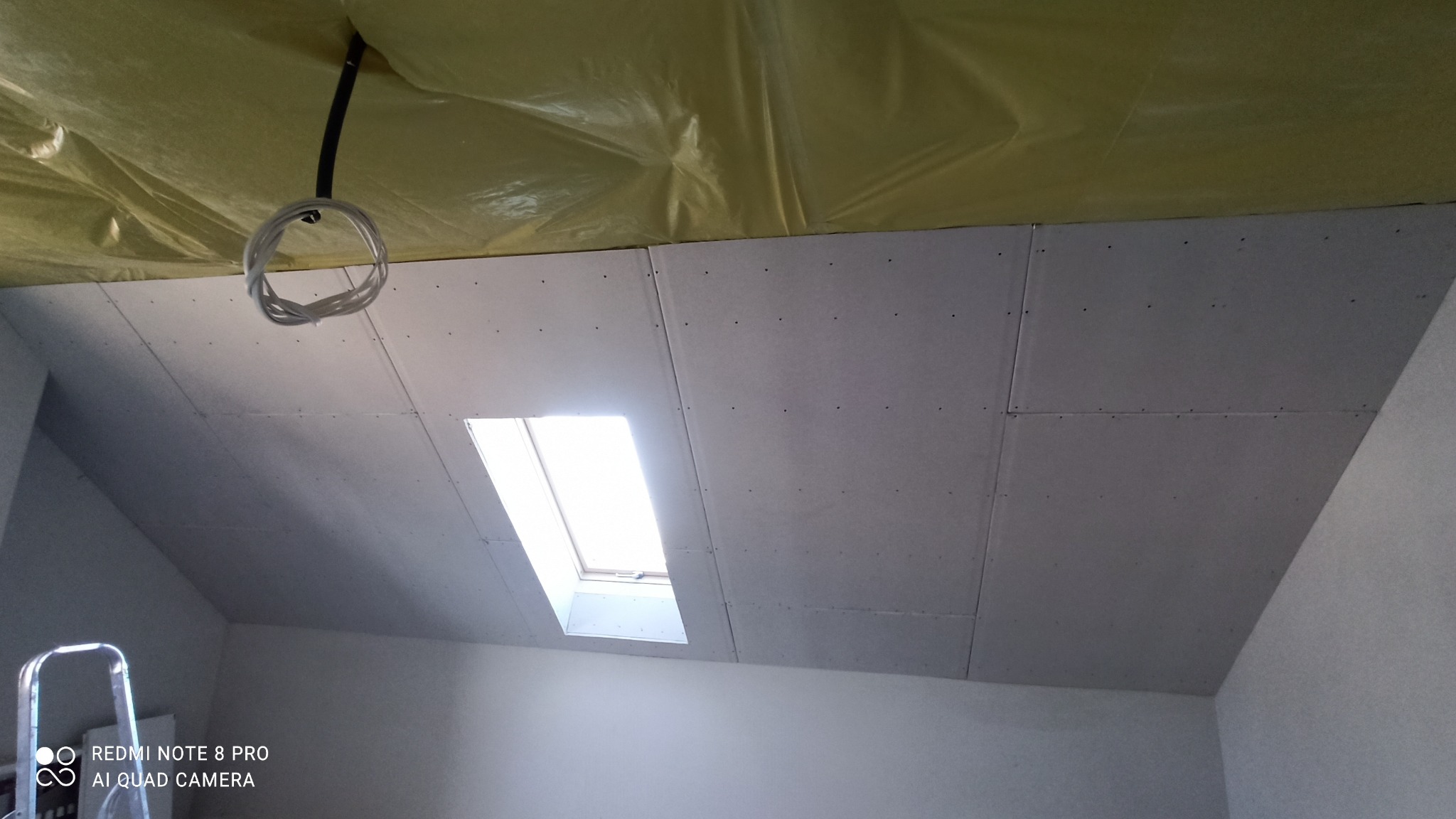 Montaż płyt na poddaszu z oknem dachowym, widoczne przewody elektryczne i drabina.