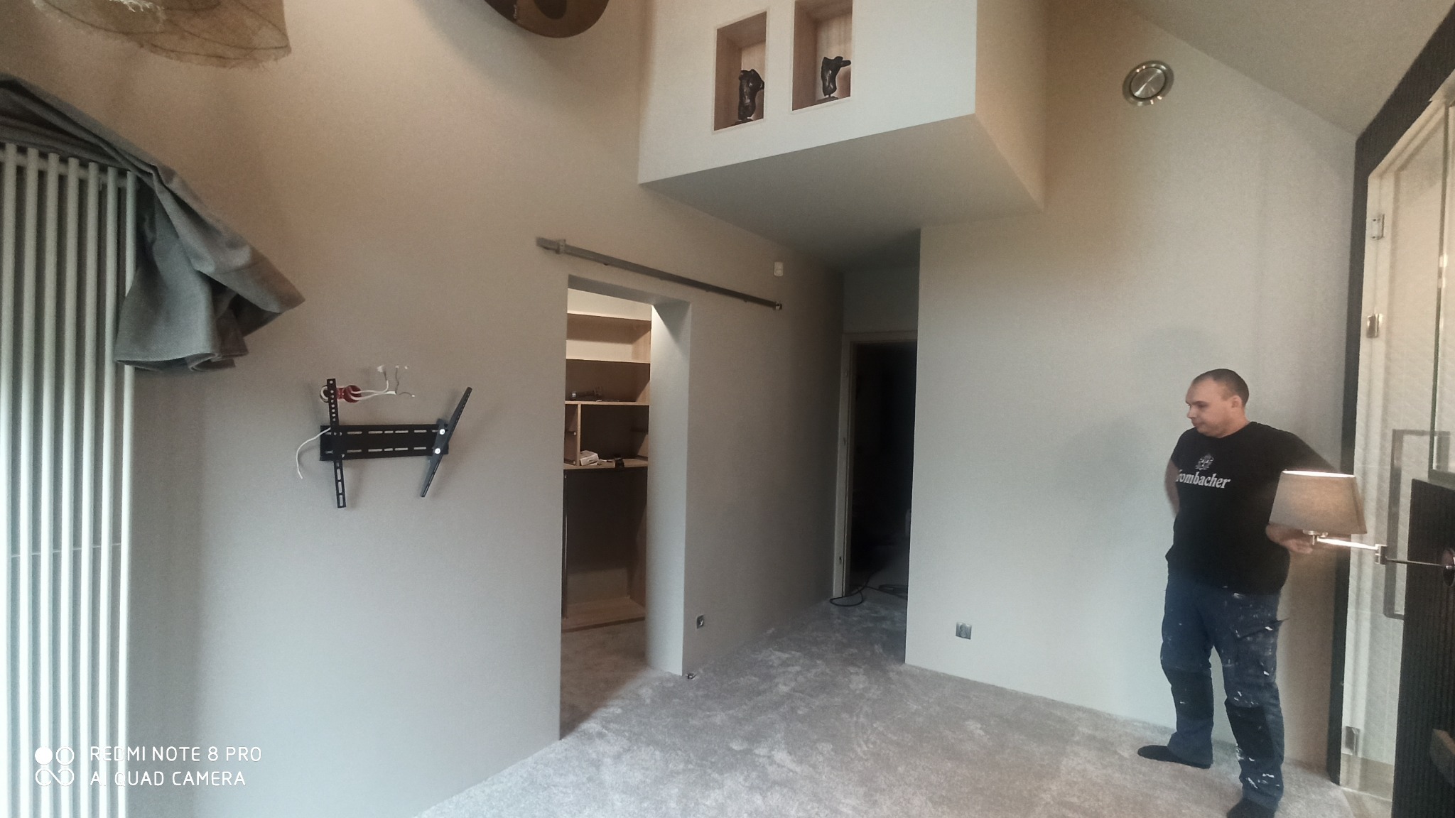 Wnętrze po odświeżeniu ścian we Wrocławiu z widocznym pracownikiem, uchwytem na telewizor na ścianie, grzejnikiem i otwartą garderobą.