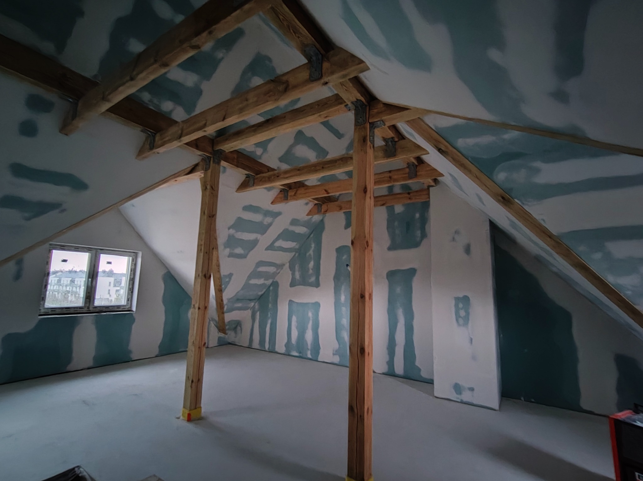 Poddasze w trakcie wykańczania: drewniana konstrukcja, ściany z płyt gipsowo-kartonowych z widocznymi łączeniami, przygotowane do dalszych prac wykończeniowych.