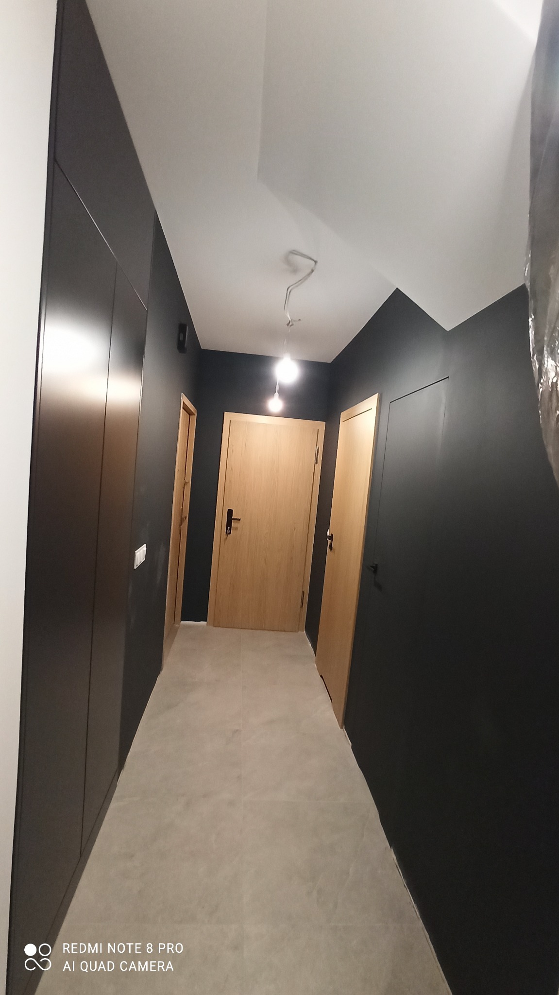 Nowoczesny korytarz we Wrocławiu po remoncie: ciemne ściany, jasna podłoga, drewniane drzwi. Minimalistyczny design z oświetleniem punktowym.