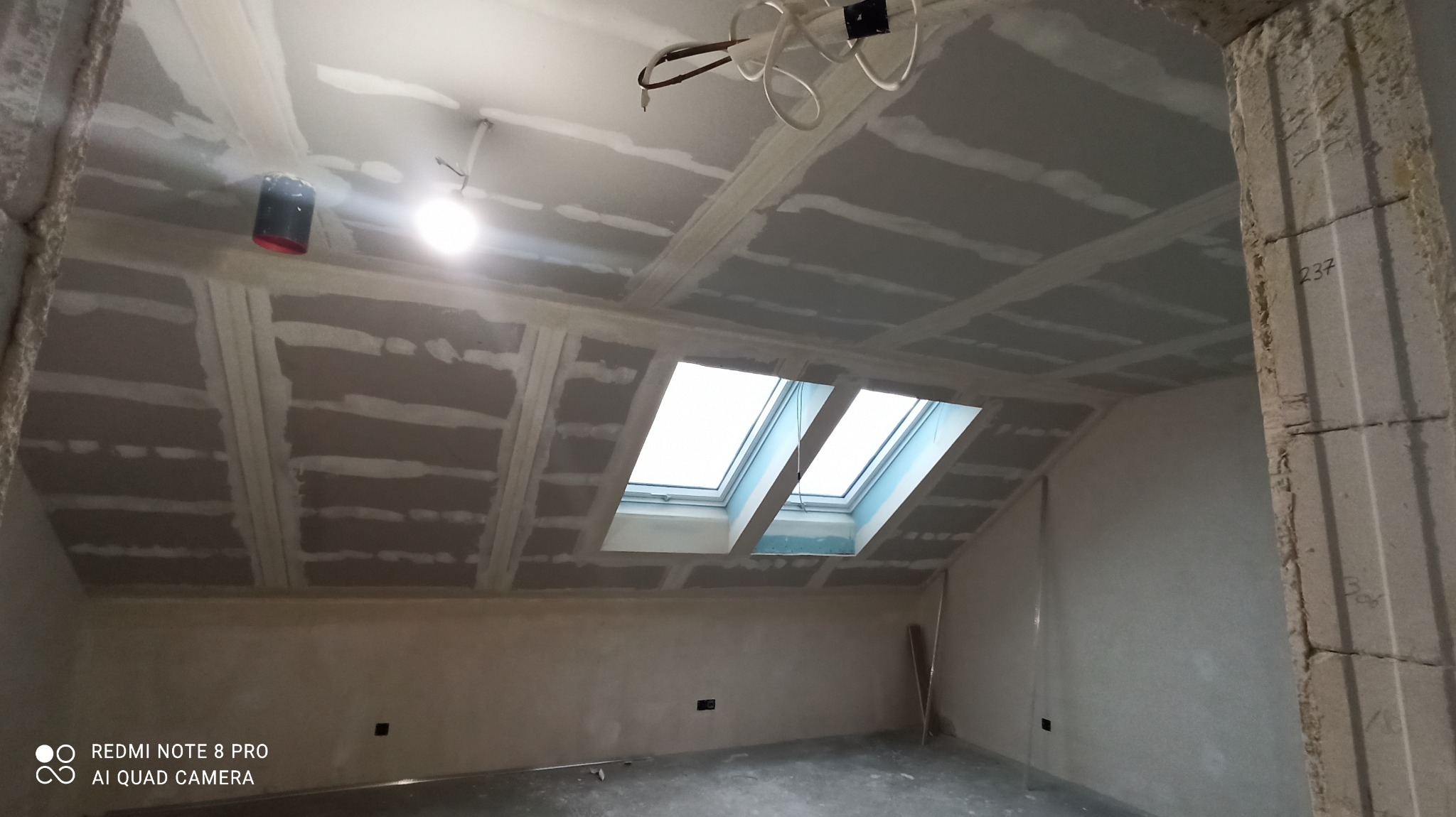 Poddasze z oknami dachowymi w trakcie montażu płyt gipsowo-kartonowych na suficie. Widoczne łączenia płyt i przygotowane otwory na oświetlenie.