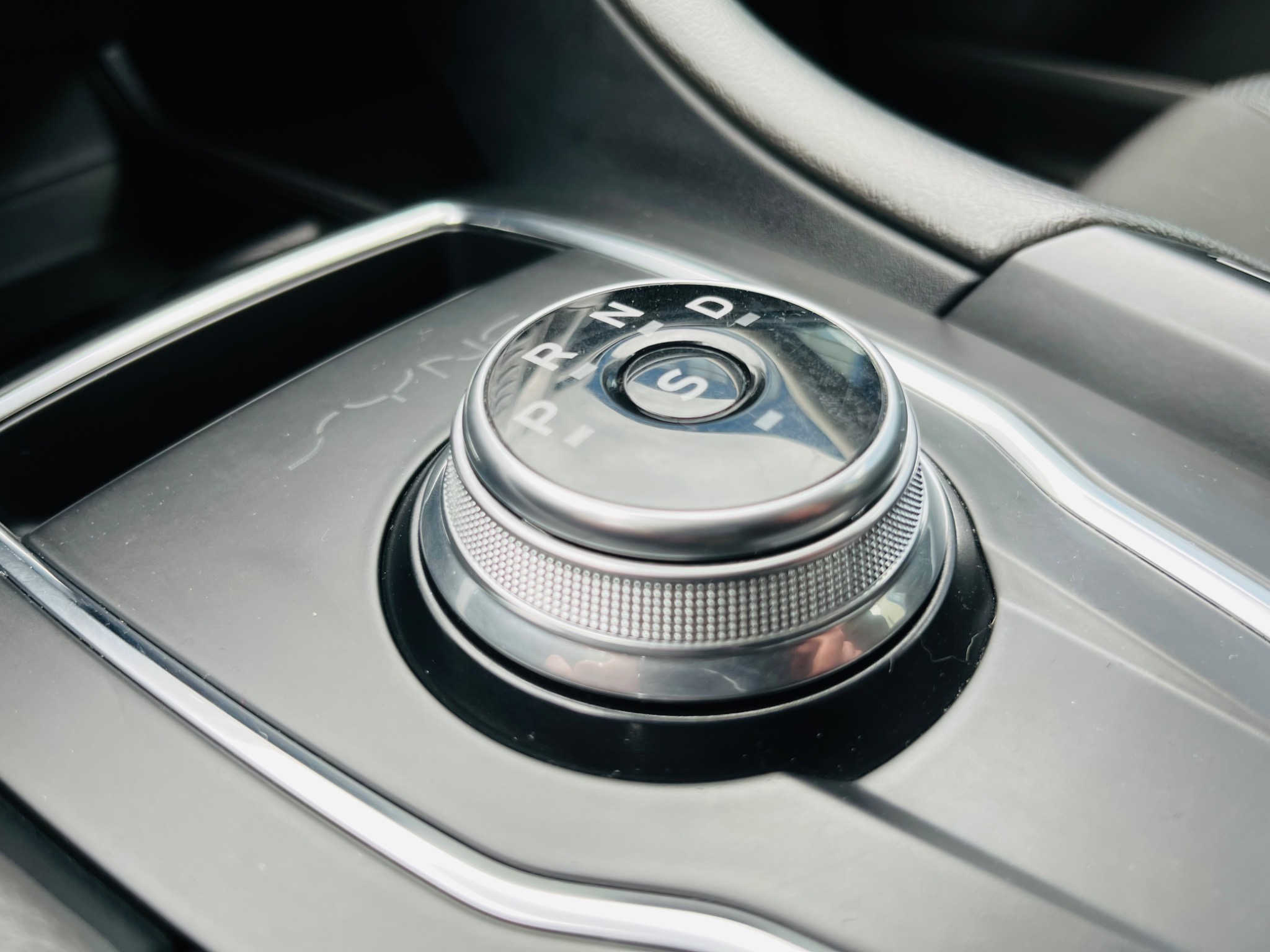 Centralny widok na okrągły selektor trybów jazdy w samochodzie z opcjami P, R, N, D, S, osadzony w czarnej konsoli.